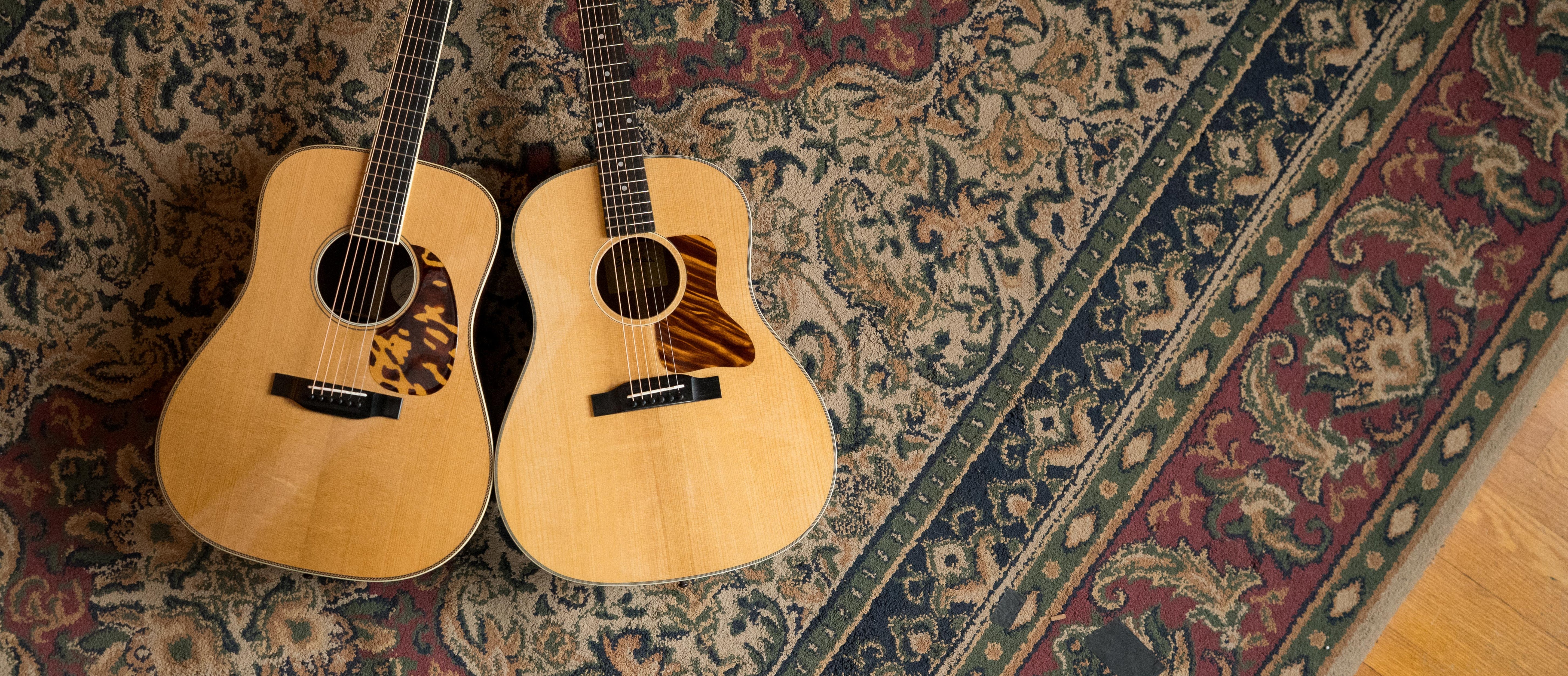 Two acoustic guitars with light wood bodies are placed side by side on an ornate, patterned rug with red, blue, and beige tones.