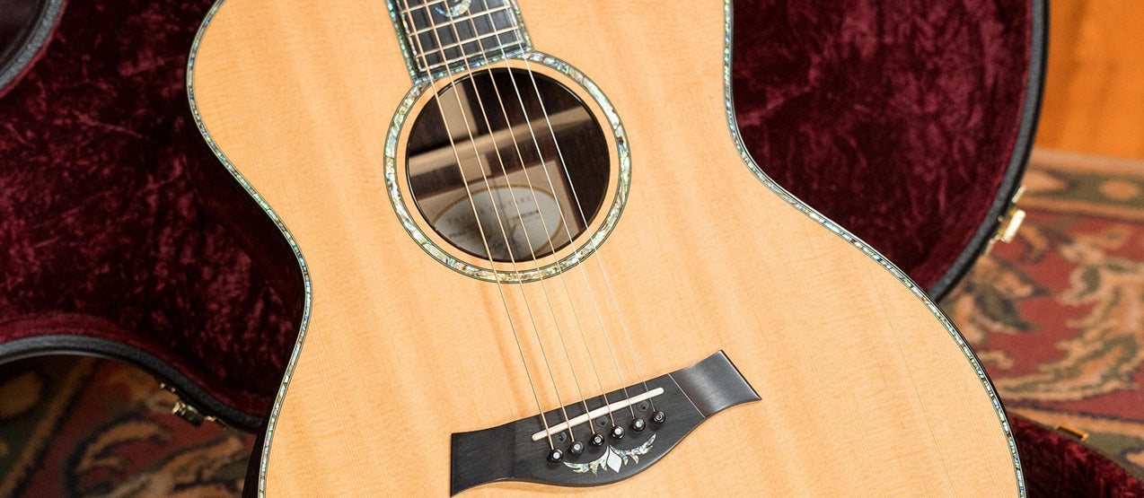 An acoustic guitar with a natural wood finish and abalone inlays is resting inside an open, plush-lined guitar case.