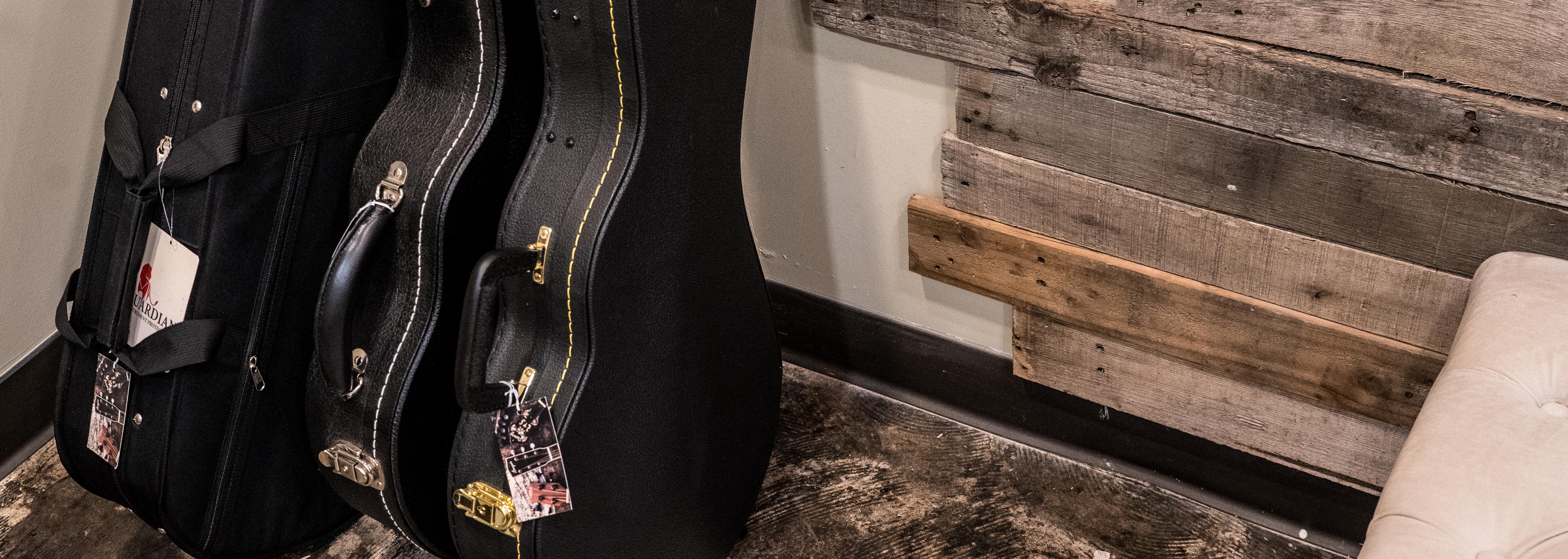 Two black instrument cases lean against a wall with rustic wooden paneling. A small section of a beige cushioned seat is visible in the lower right corner. The floor is a dark, textured surface.
