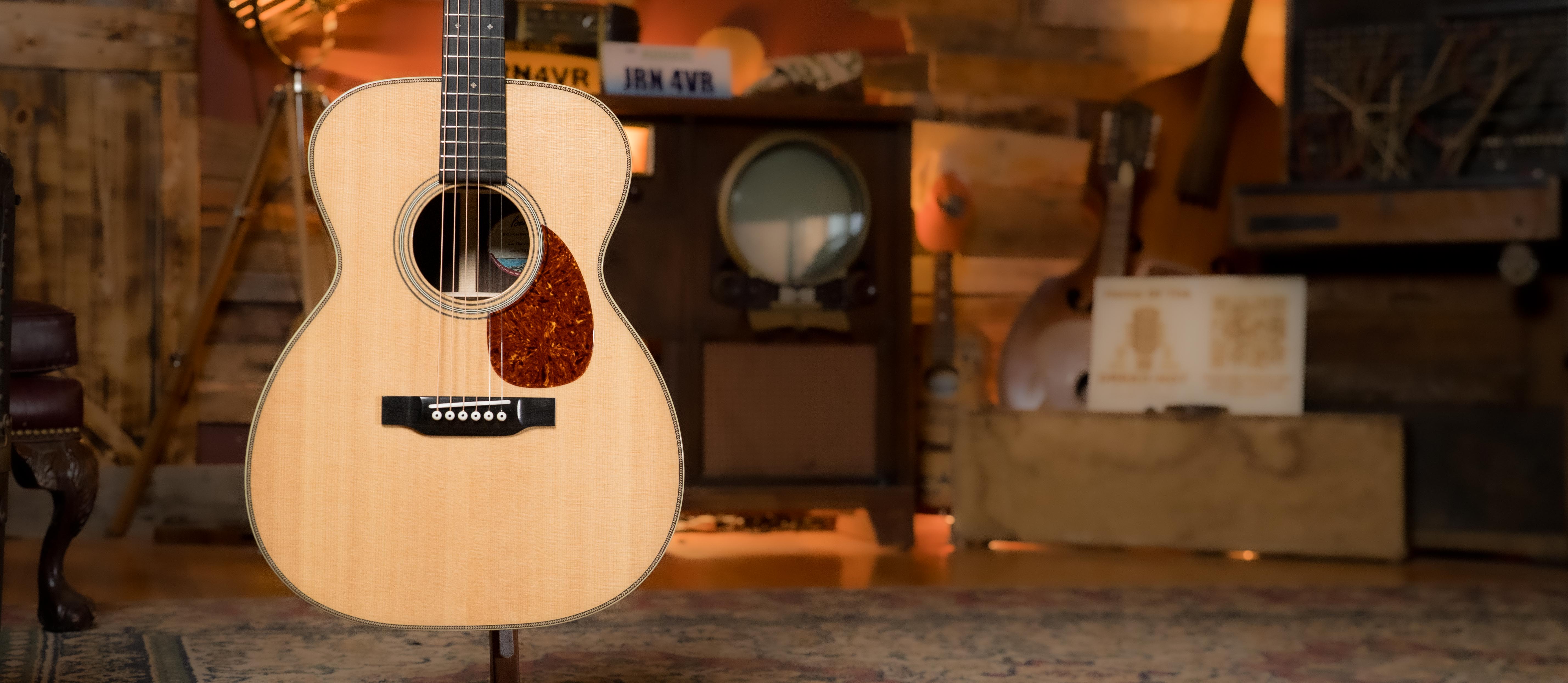 An acoustic guitar on a stand in a cozy, rustic room with vintage furniture, wooden walls, and warm lighting in the background.
