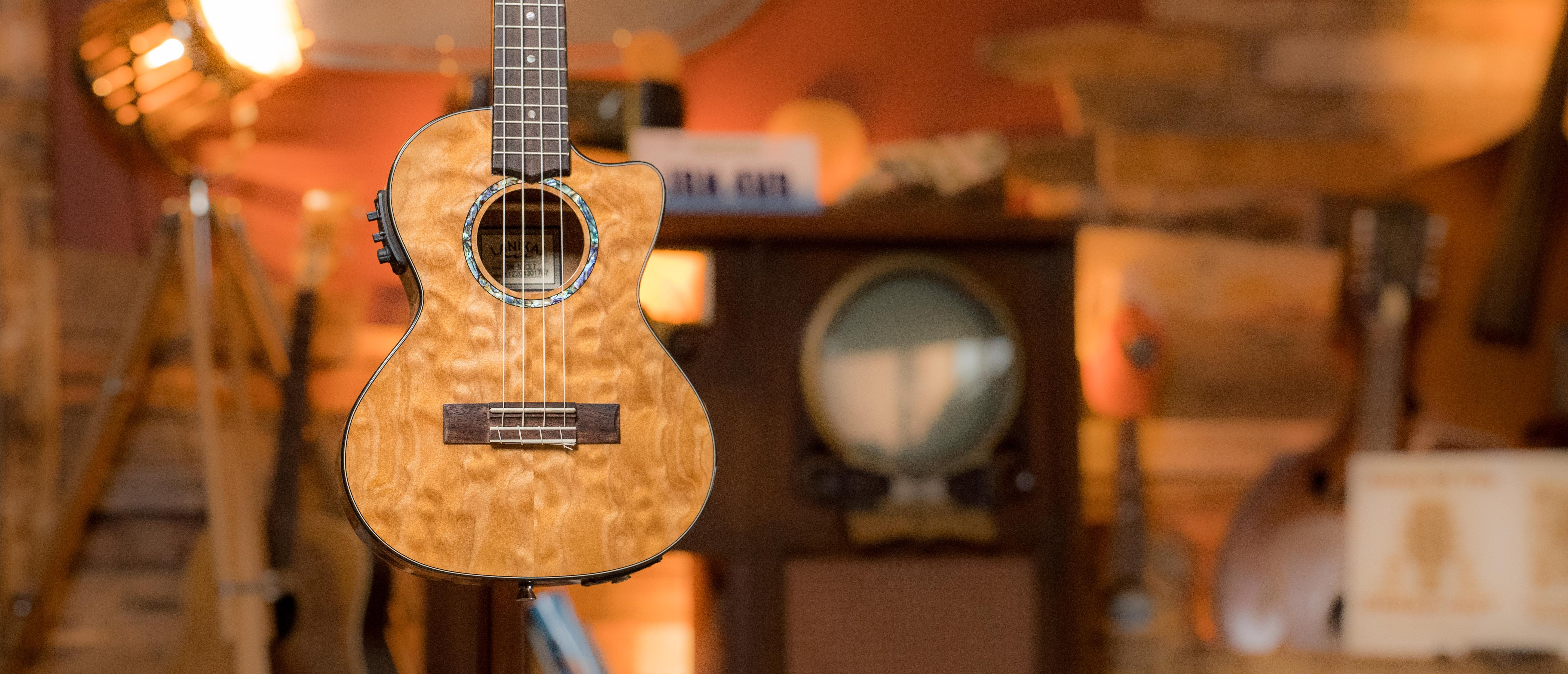A close-up of an acoustic guitar with a natural wood finish, suspended in front of a blurred background featuring vintage decor and musical instruments.