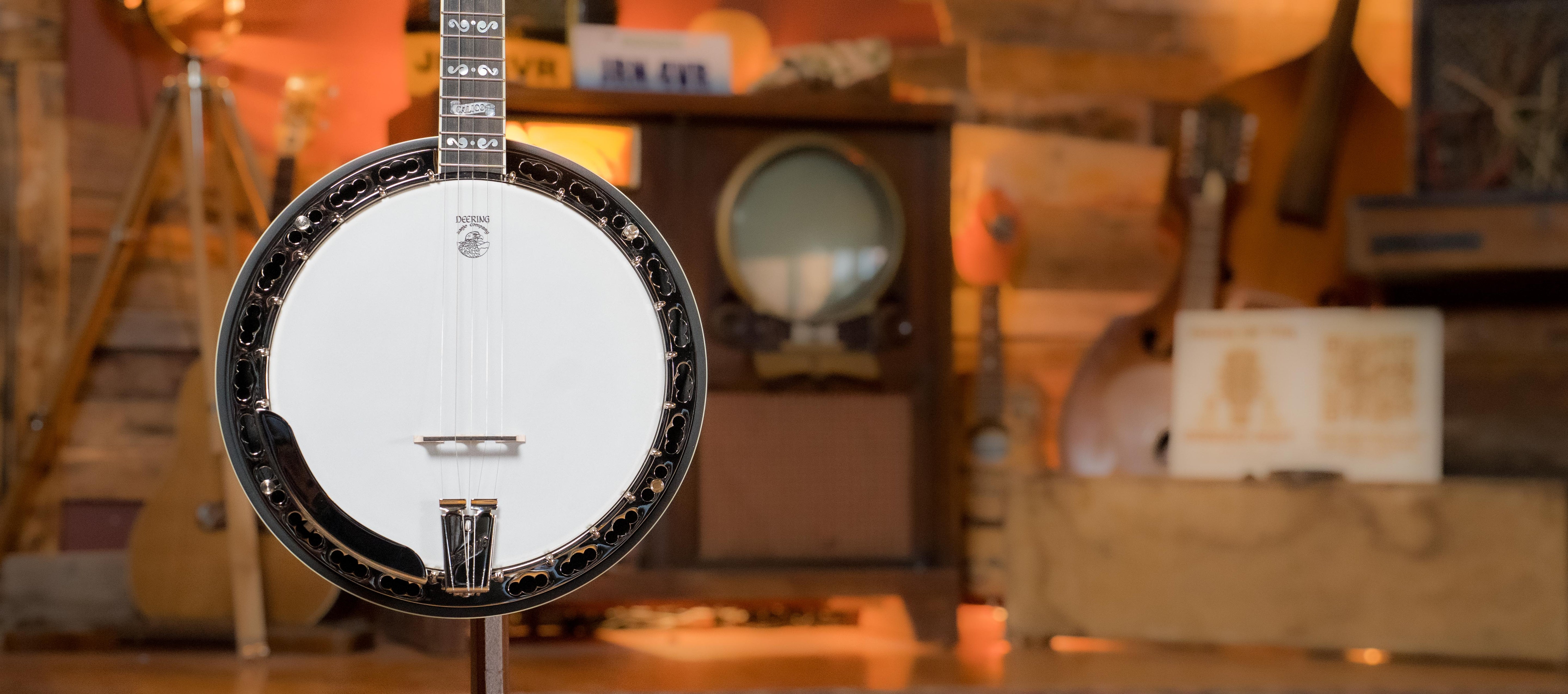 A close-up of a banjo on a stand in a rustic room, with a vintage TV and musical instruments blurred in the background.