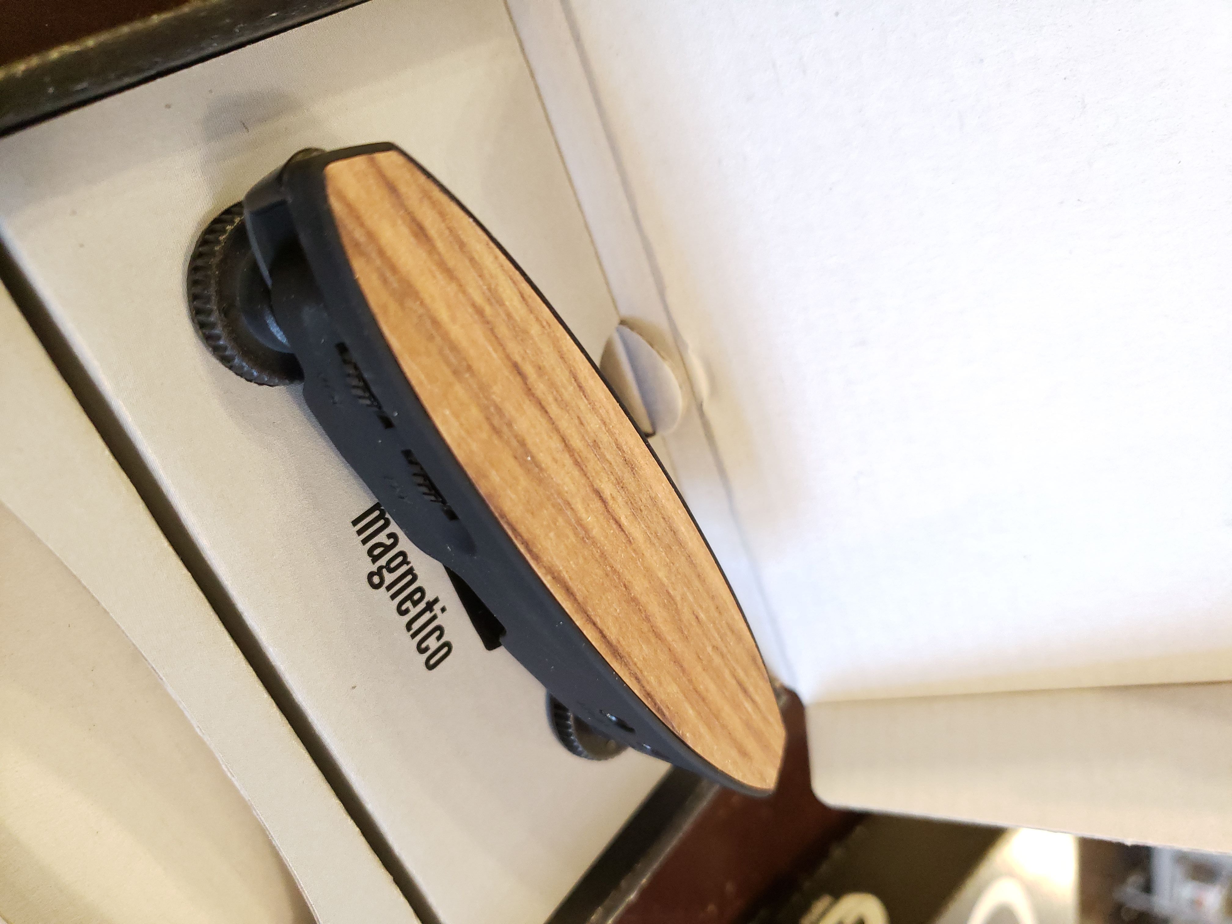 A compact skateboard with a wood deck and black wheels sits in a white box labeled Magnetico, echoing the innovative design of The Acoustic Shoppe’s Schertler Magnetico M-AG6-LIMITED acoustic guitar magnetic soundhole pickup (light wood top).