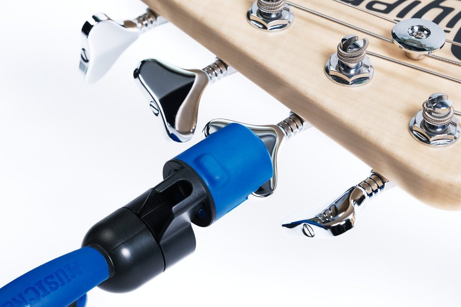 A close-up of a light wood guitar headstock with the Music Nomad GRIP ONE (MN223)—an all-in-one blue and black string winder, cutter, and puller—attached to one of the shiny metal tuning pegs.