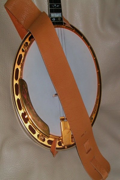 A close-up of a banjo with a golden rim features the Lakota 3SPNB Spruce 3 Banjo Non Cradle Strap draped across its body, set against a light textured background.