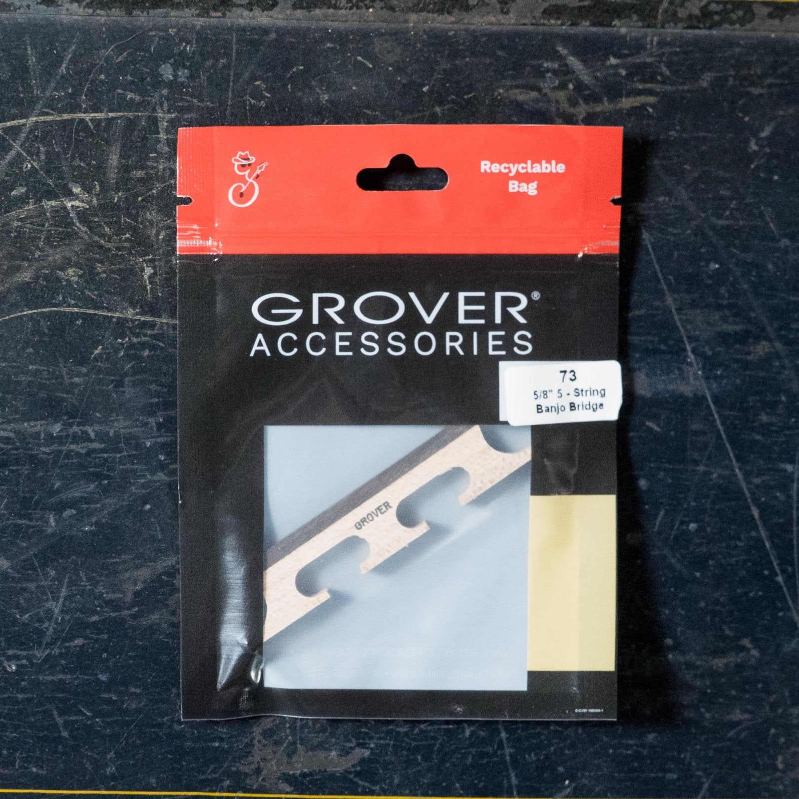 A Grover 73 5-String 5/8 Banjo Bridge is packaged in mostly black and red Grover Accessories packaging with a clear window, showing the maple bridge inside and labeled as a 5-string 5/8 banjo bridge.
