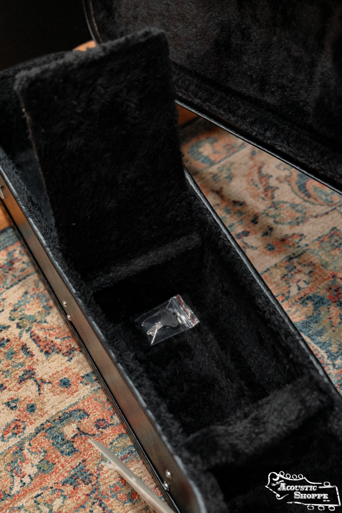 An open Guardian CG-022-OOO Deluxe Hardshell Case-000 Style, velvet-lined and black, rests on a patterned rug with a small plastic bag inside—the quality youd expect from Guardian.