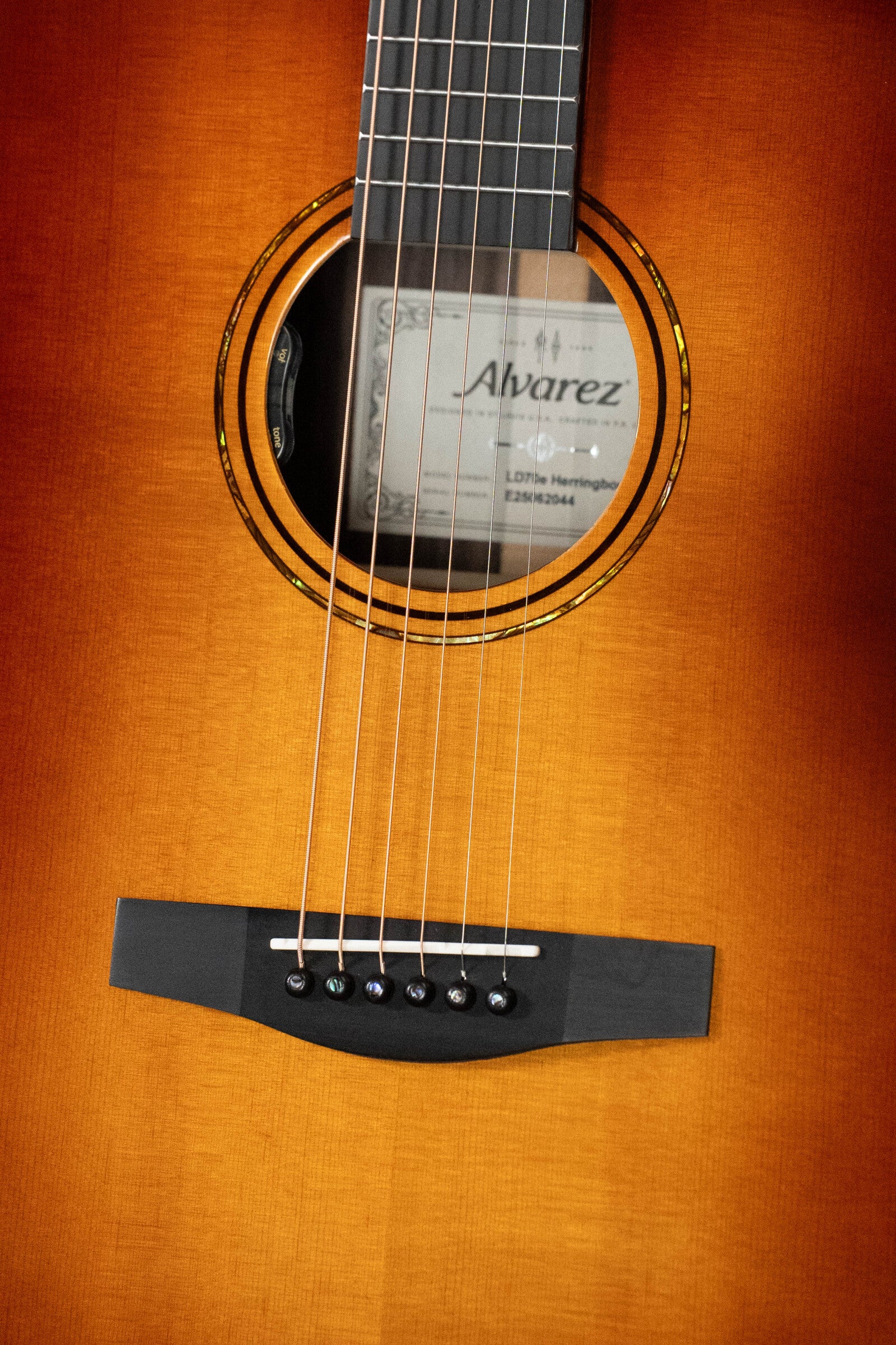Close-up of the Alvarez Laureate Series LD70e Herringbone Sunset Sitka/Rosewood Dreadnought Guitar with LR Baggs Hifi Pickup, showing strings, soundhole, label, and bridge in a warm sunburst finish.