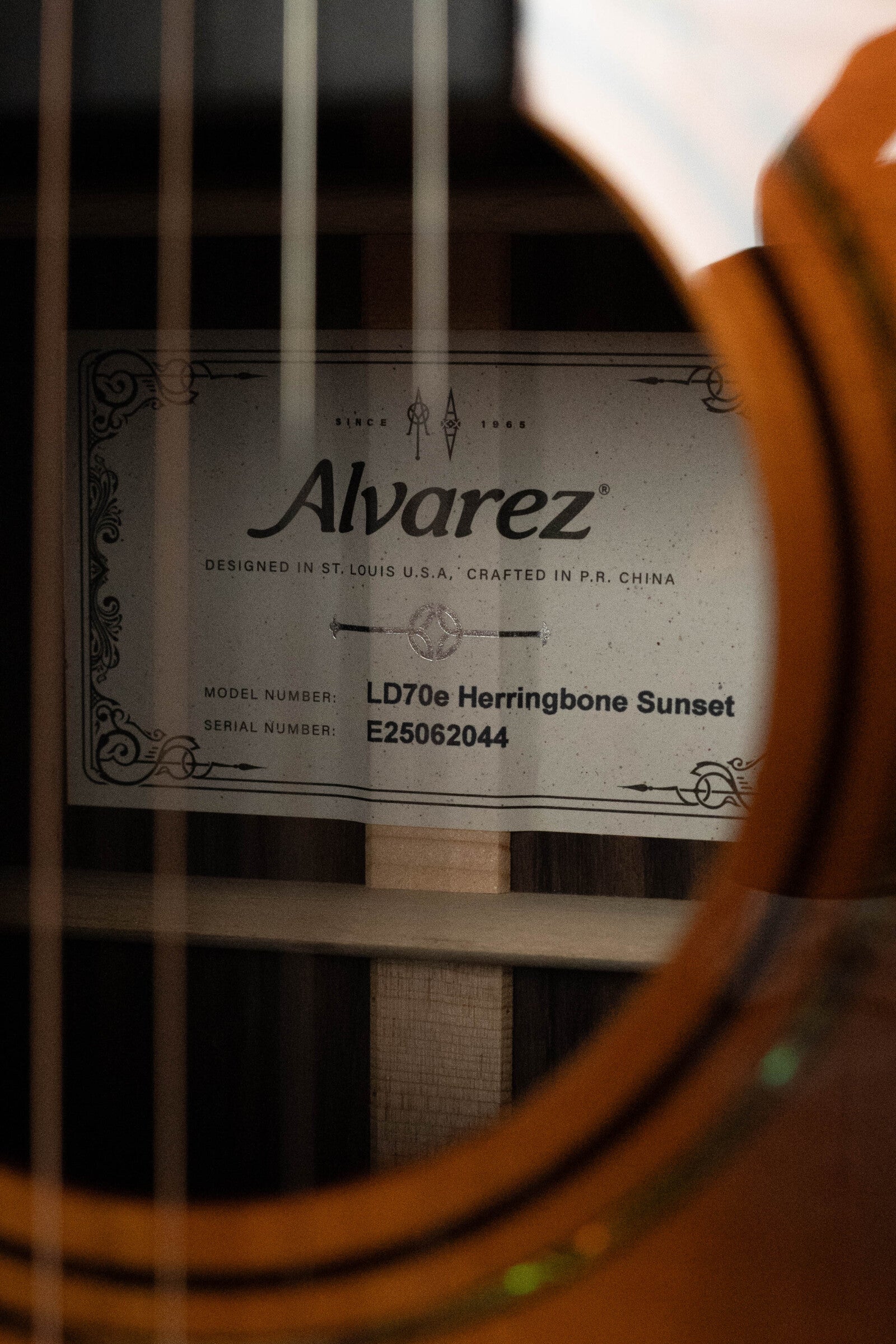 Close-up of the Alvarez Laureate Series LD70e Herringbone Sunset Sitka/Rosewood Dreadnought Guitar label (#2044) seen through the sound hole, displaying brand, model, serial number, and LR Baggs HiFi pickup reference.