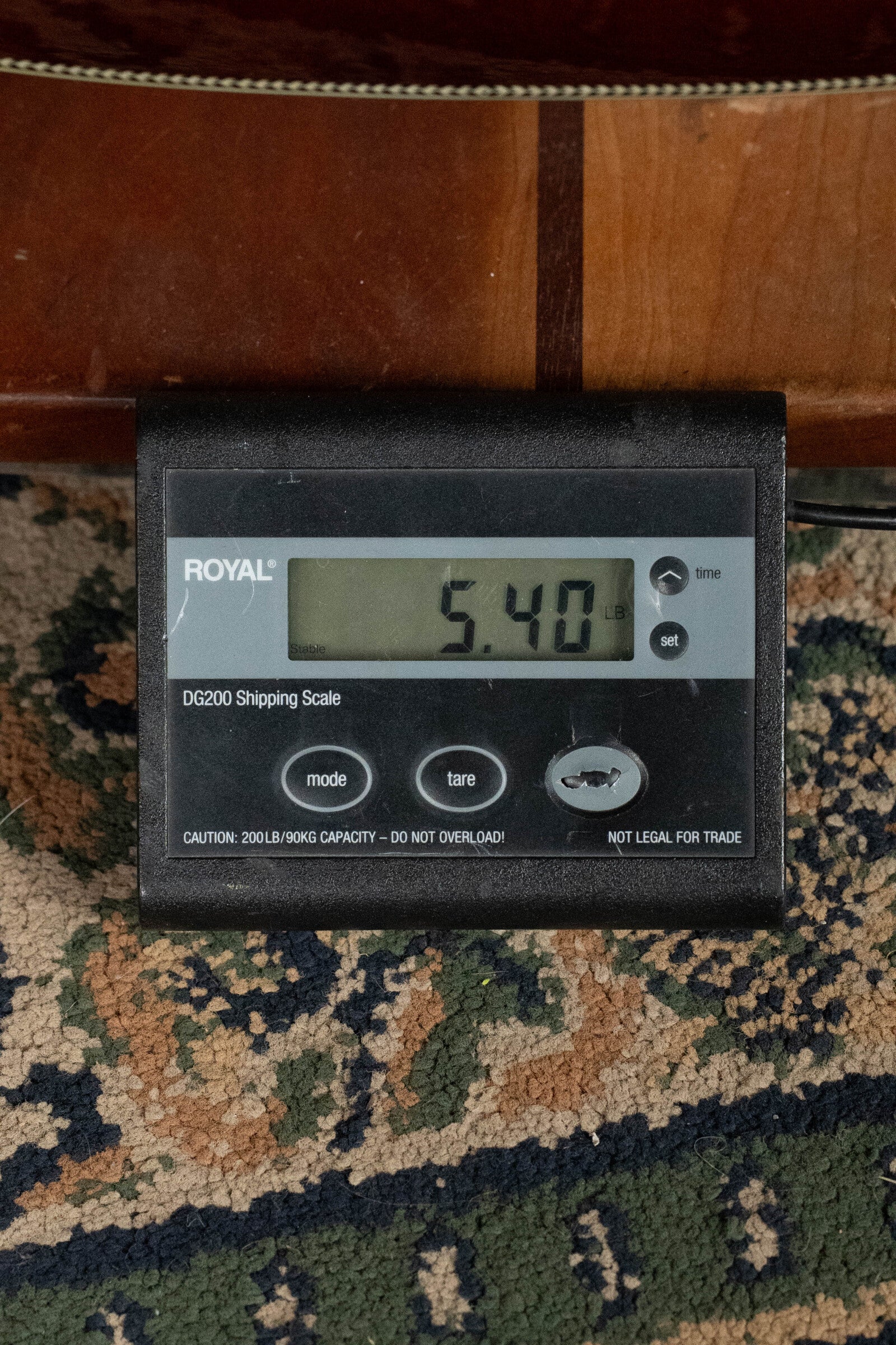 A digital shipping scale shows 5.40 pounds. The black scale sits on a patterned carpet, with part of the Alvarez Laureate Series LD70e Herringbone Sunset Sitka/Rosewood Dreadnought Guitar w/LR Baggs HiFi visible above.