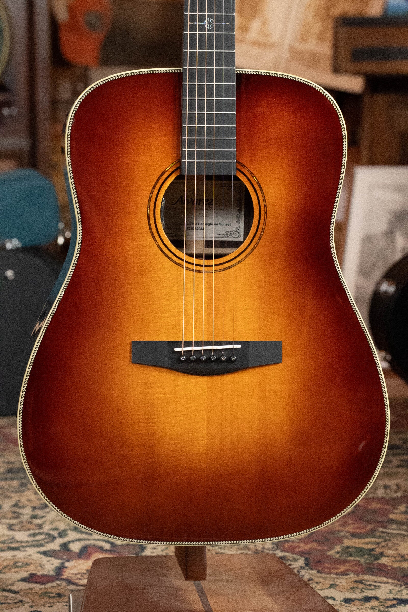 The Alvarez Laureate Series LD70e Herringbone Sunset Sitka/Rosewood Dreadnought Guitar w/LR Baggs Hifi Pickup (#2044) features a sunburst finish fading to amber, dark bridge, and elegant details, shown indoors on a patterned rug.