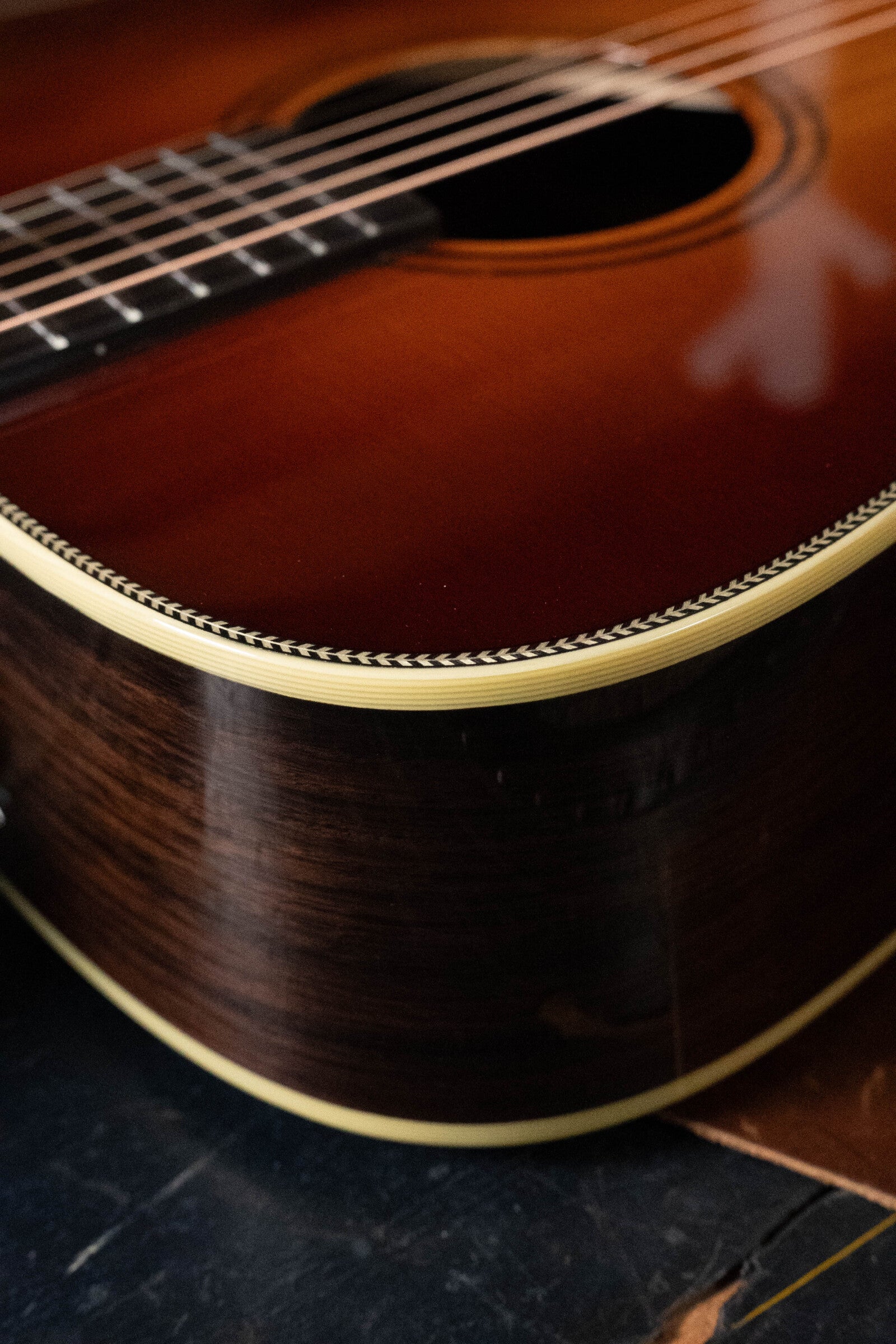 Close-up of the Alvarez Laureate Series LD70e Herringbone Sunset Sitka/Rosewood Dreadnought Guitar with LR Baggs Hifi Pickup, highlighting its strings, wood finish, and herringbone binding on a dark surface.