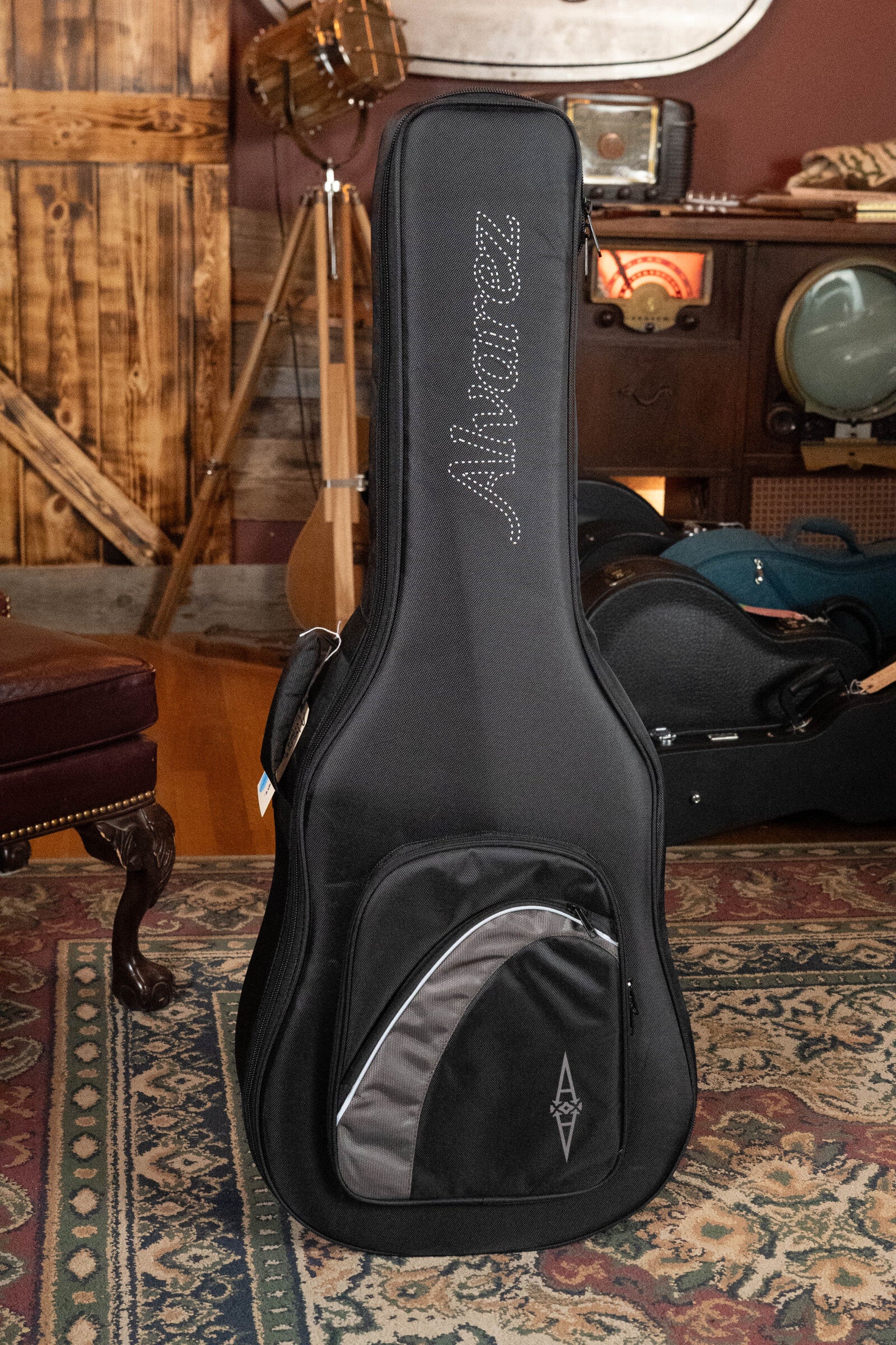 An Alvarez Laureate Series LD70e Herringbone Sunset Sitka/Rosewood Dreadnought Guitar with LR Baggs Hifi Pickup (#2044) rests upright in a cozy, vintage-themed room with musical instruments and decor visible in the background.