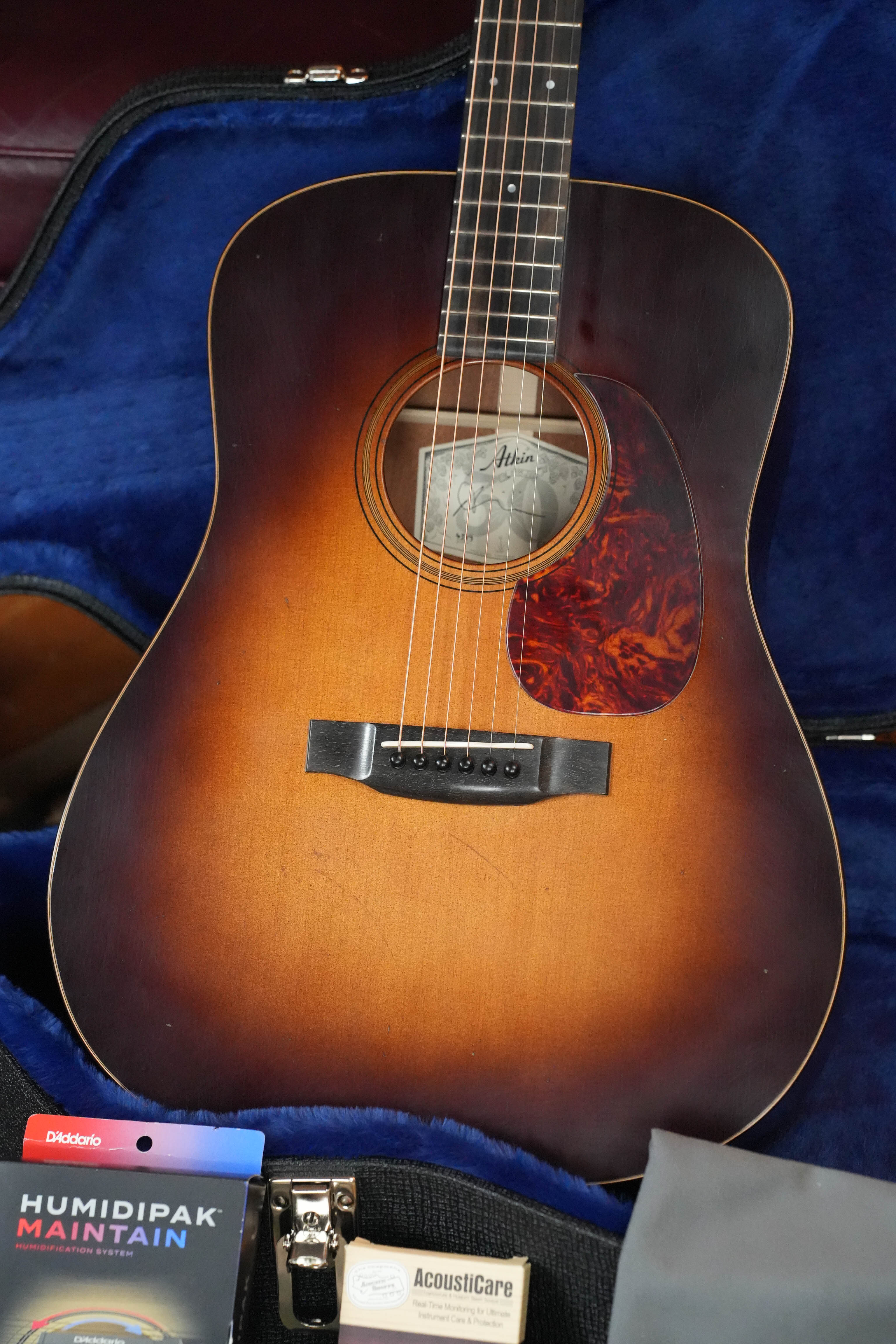 An Atkin Essential D 45MM Sitka/Mahogany Dreadnought Acoustic Guitar (#4399) by Atkin Guitars rests in an open blue-lined case, with a humidipak and cleaning cloth visible in the foreground.