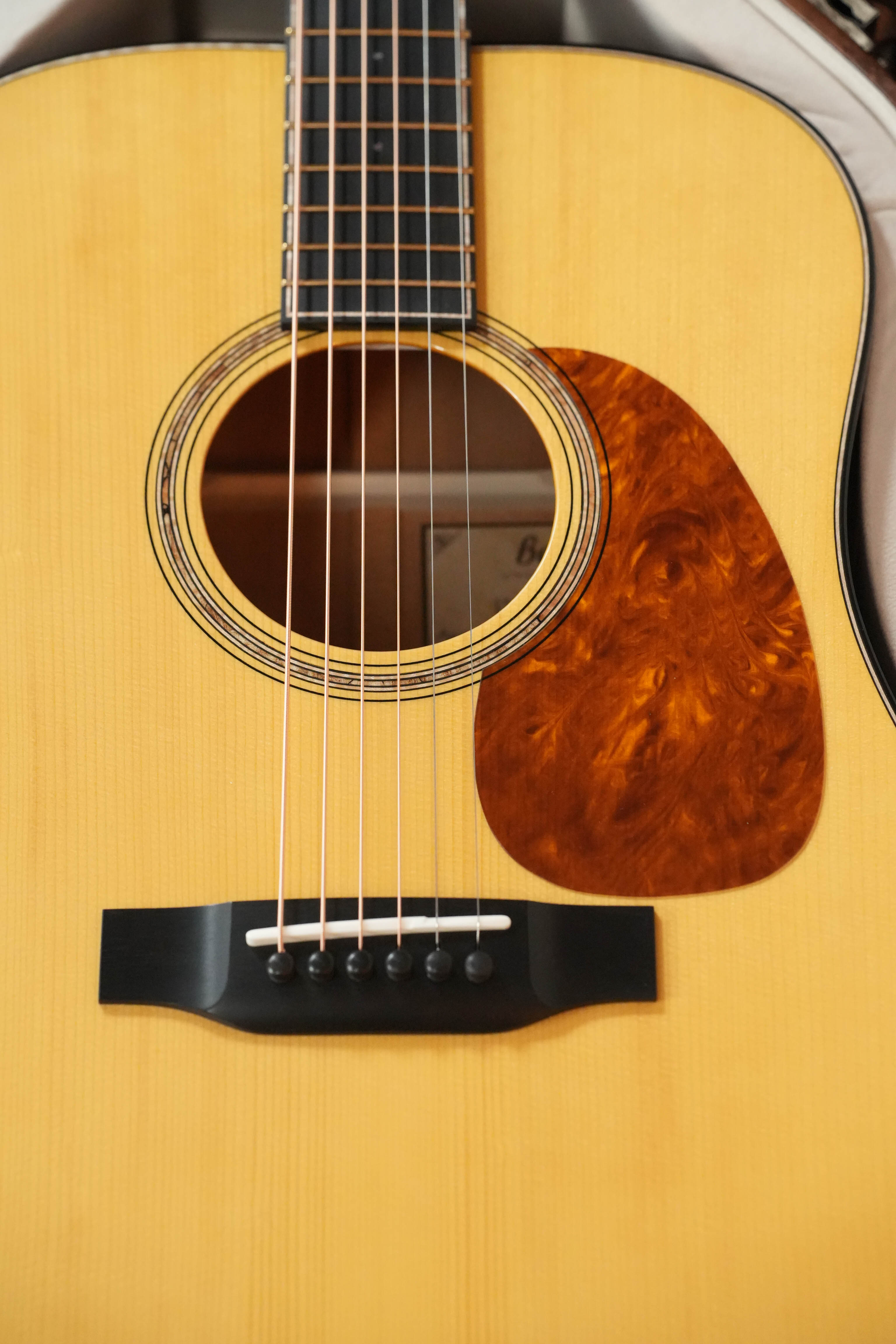 Close-up of a Bedell Guitars Special Edition 1940 Dreadnought Narrow Nut Acoustic Guitar #5004, featuring strings, a decorative sound hole ring, brown marbled pickguard, and Adirondack spruce top on a light wood body.