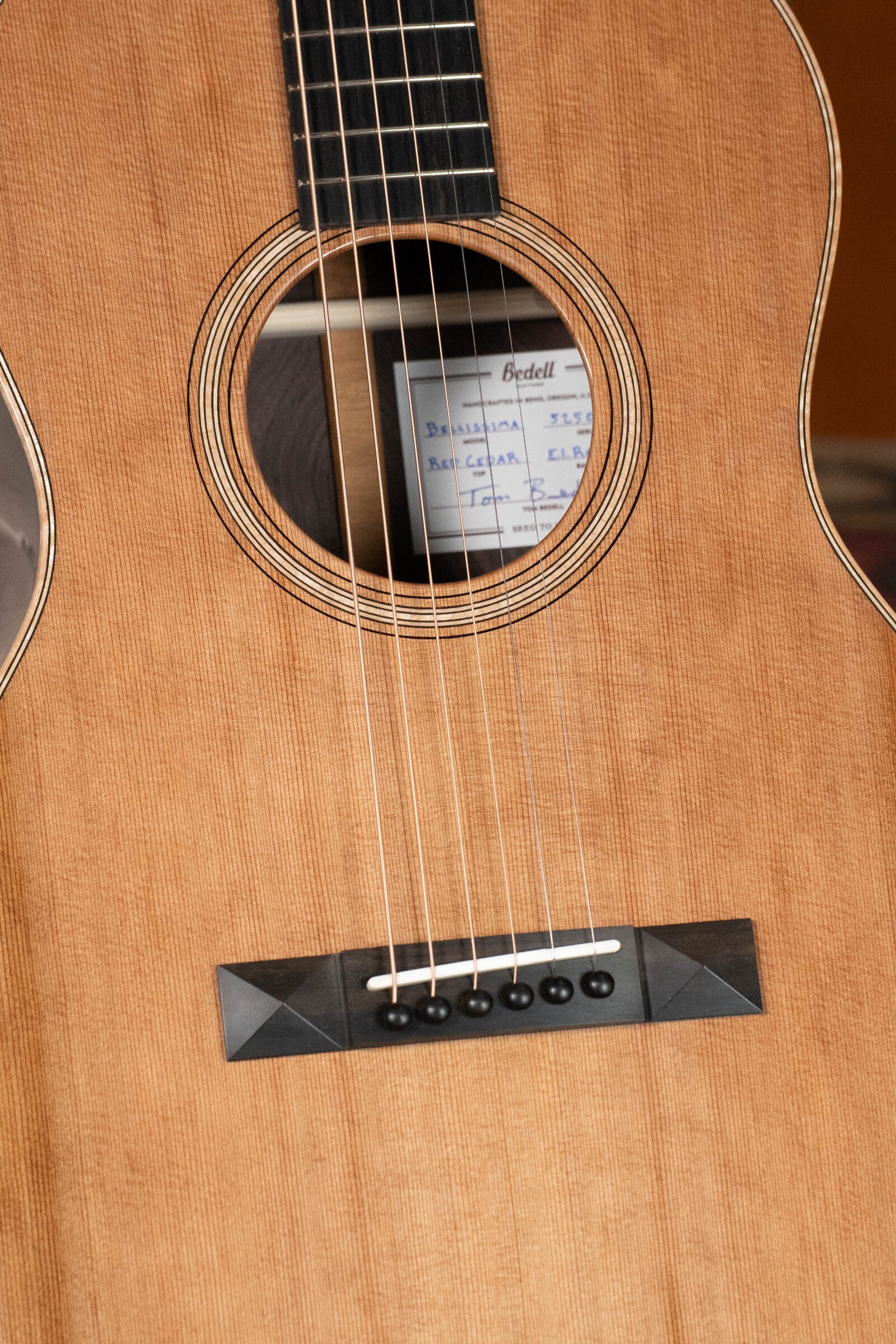 Close-up of the Bedell Guitars Angelica Bellissima Red Cedar/Rosewood Parlor Guitar w/K&K Pure Mini Pickup (#5002), highlighting the soundhole, strings, and bridge with visible paper label—ideal for fingerstyle guitarists.