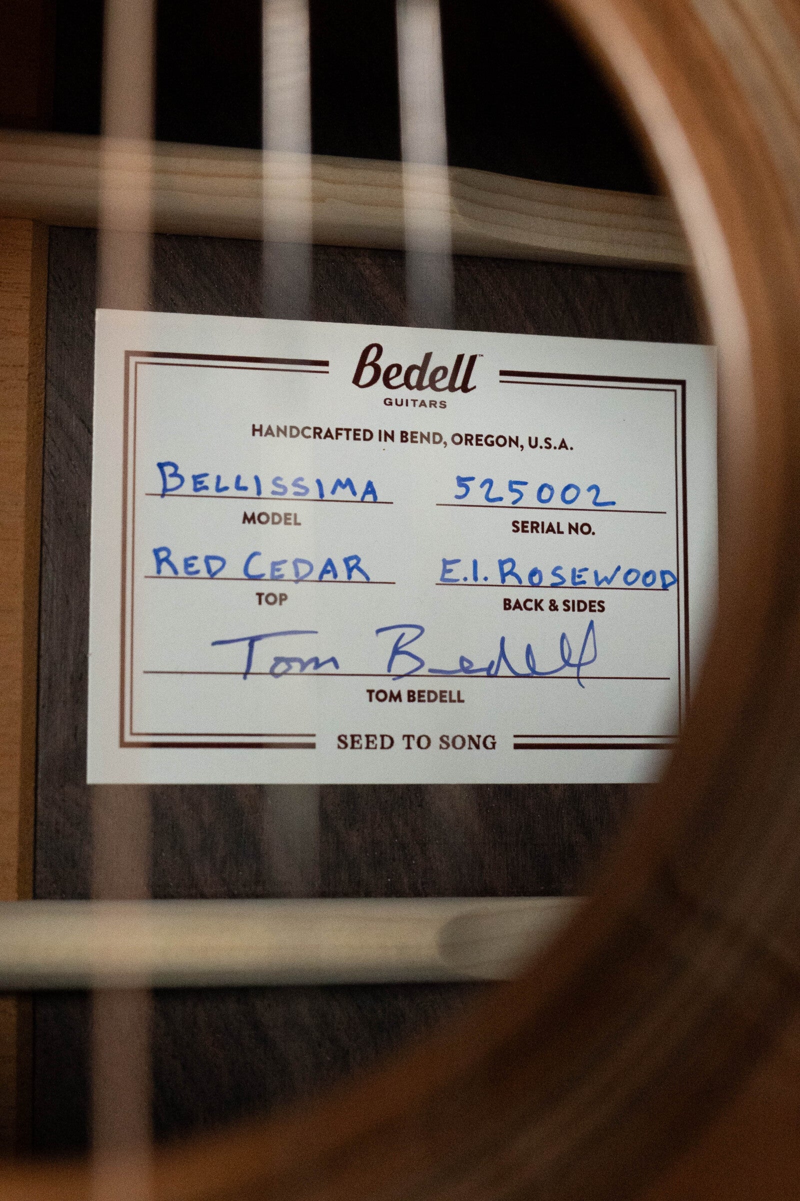 A close-up through the strings reveals a Bedell Guitars label inside an Angelica Bellissima Red Cedar/Rosewood Parlor Guitar w/K&K Pure Mini Pickup, #5002, featuring a red cedar top and rosewood back and sides.