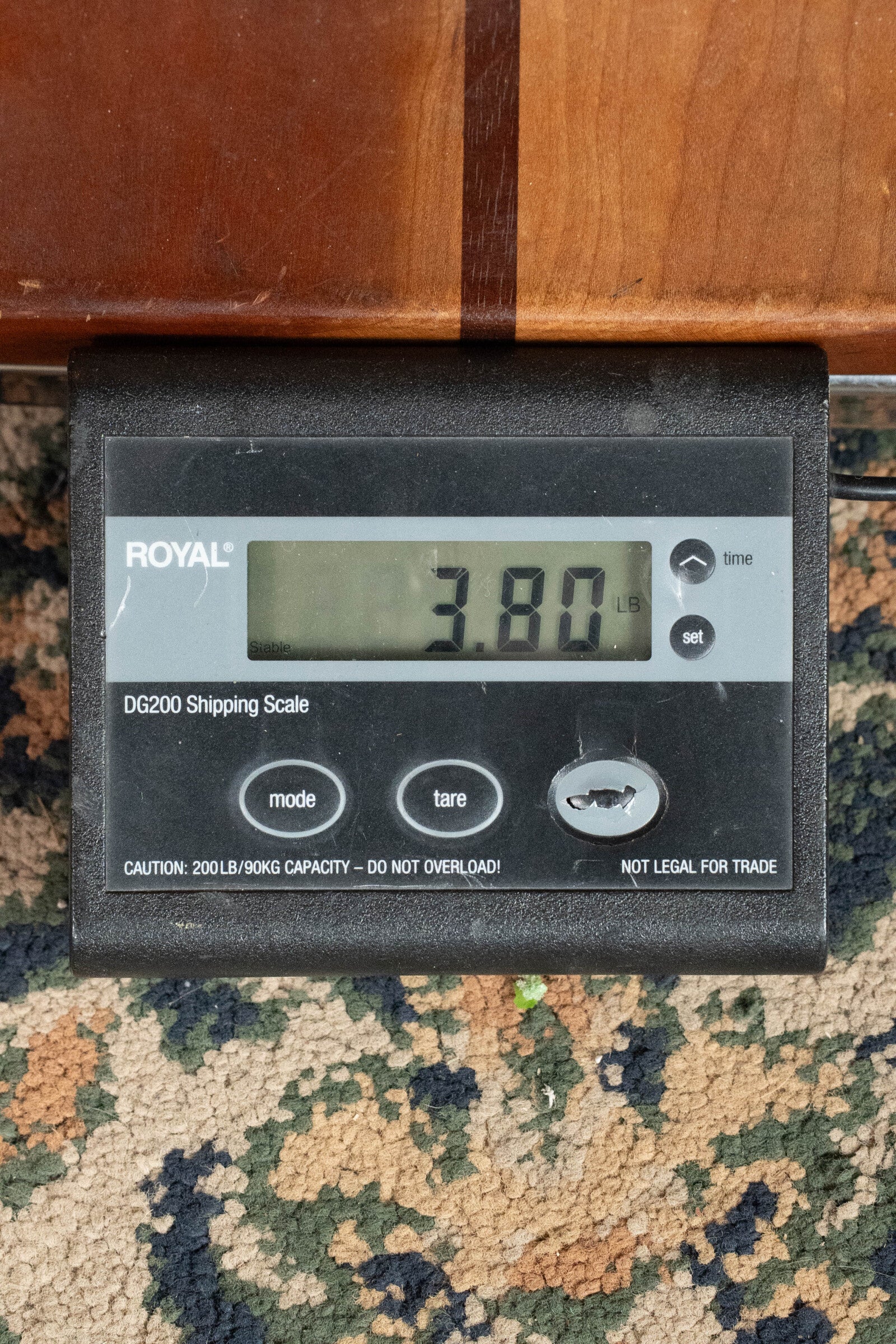 A Bedell Guitars Angelica Bellissima Red Cedar/Rosewood Parlor Guitar w/K&K Pure Mini Pickup (#5002) weighs 3.80 pounds on a digital scale, shown on a patterned carpet beside a wooden surface.