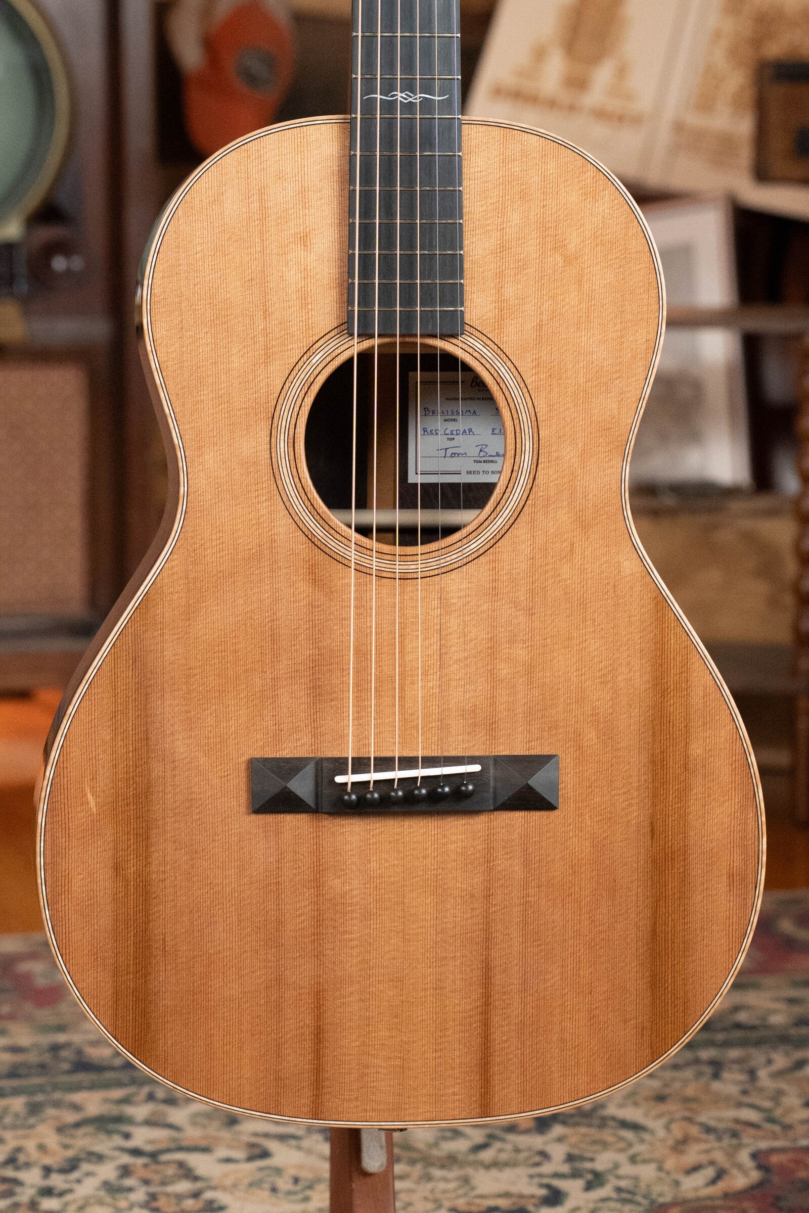 A close-up of the Bedell Guitars Angelica Bellissima Red Cedar/Rosewood Parlor Guitar w/K&K Pure Mini Pickup #5002, featuring a natural wood finish, round sound hole, black bridge, and six strings—perfect for fingerstyle players.