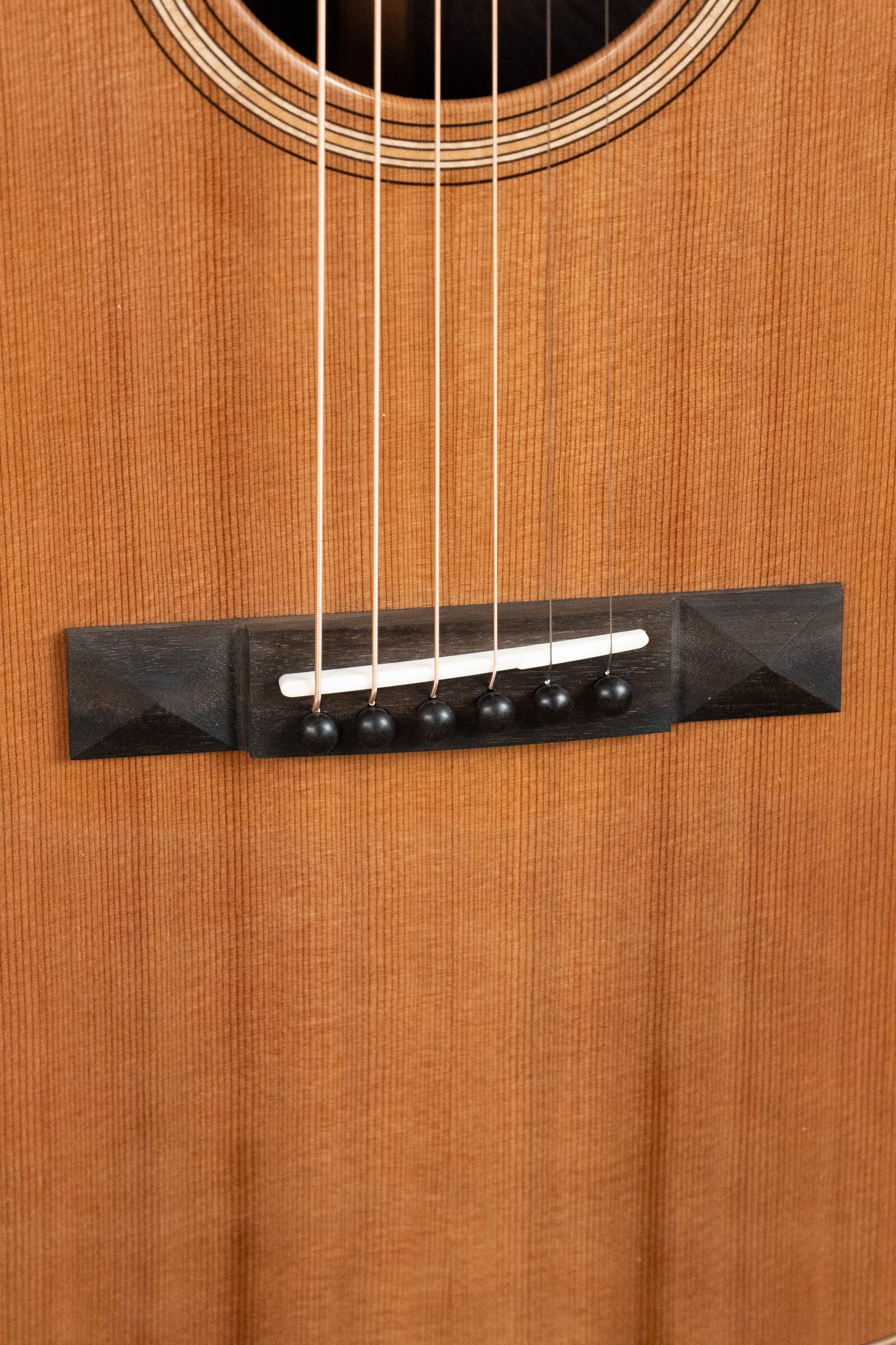 Close-up of the Bedell Guitars Angelica Bellissima Red Cedar/Rosewood Parlor Guitar w/K&K Pure Mini Pickup #5002 bridge—featuring six strings, black pins, and a white saddle on its stunning cedar/rosewood body. Perfect for fingerstyle players.