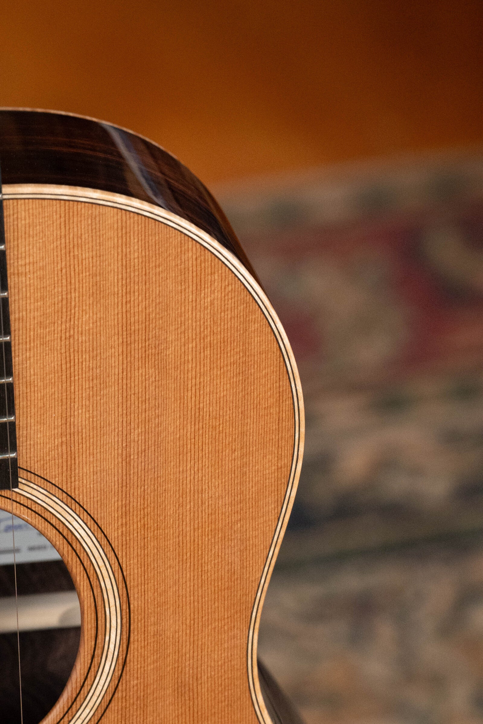 Close-up of the Bedell Guitars Angelica Bellissima Red Cedar/Rosewood Parlor Guitar w/K&K Pure Mini Pickup #5002, highlighting its wooden texture, curved edge, and sound hole over a blurred patterned carpet—ideal for fingerstyle.