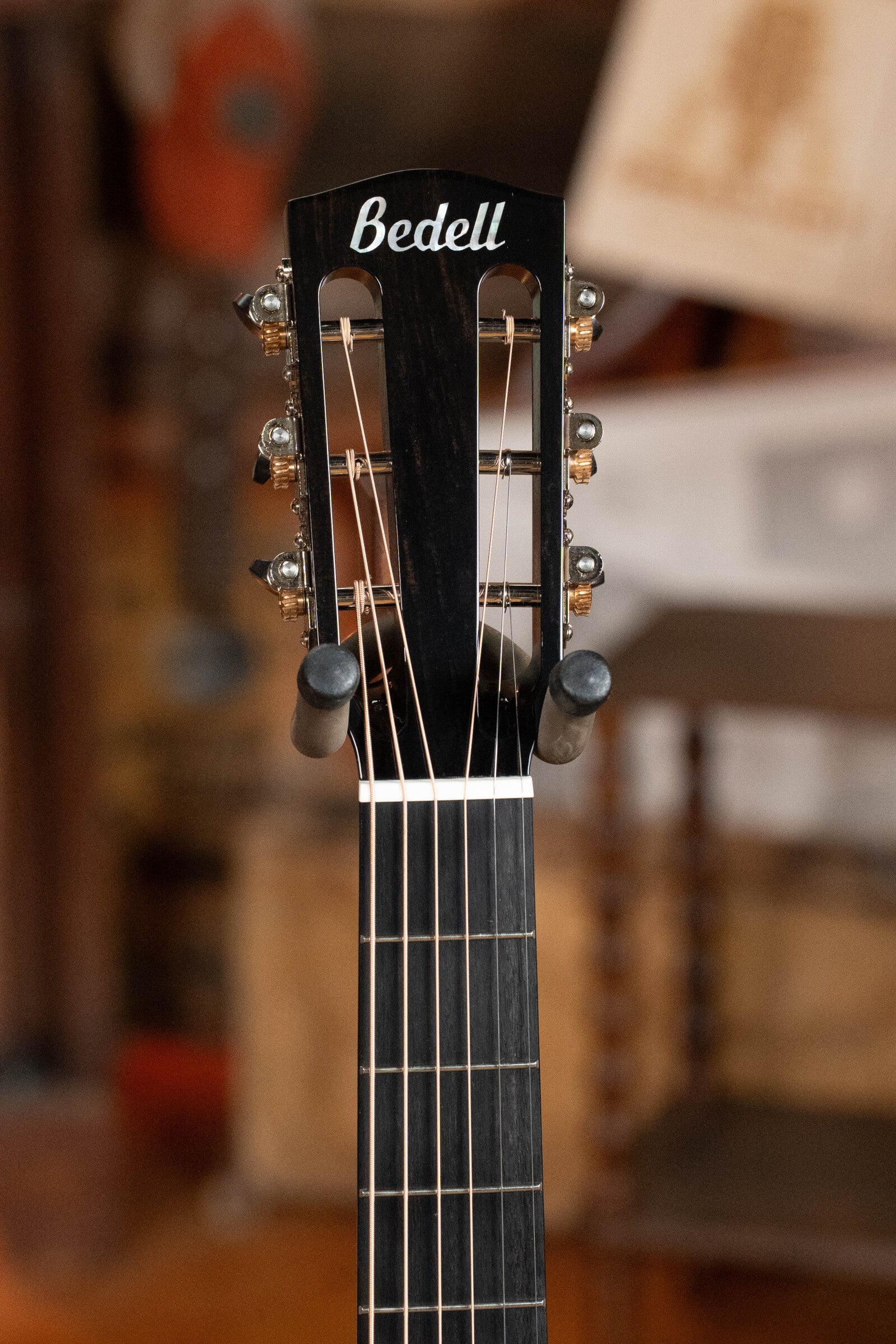 Close-up of the headstock of a Bedell Angelica Bellissima Red Cedar/Rosewood Parlor Guitar w/K&K Pure Mini Pickup #5002 by Bedell Guitars, featuring tuning pegs and strings, with a blurred indoor background.