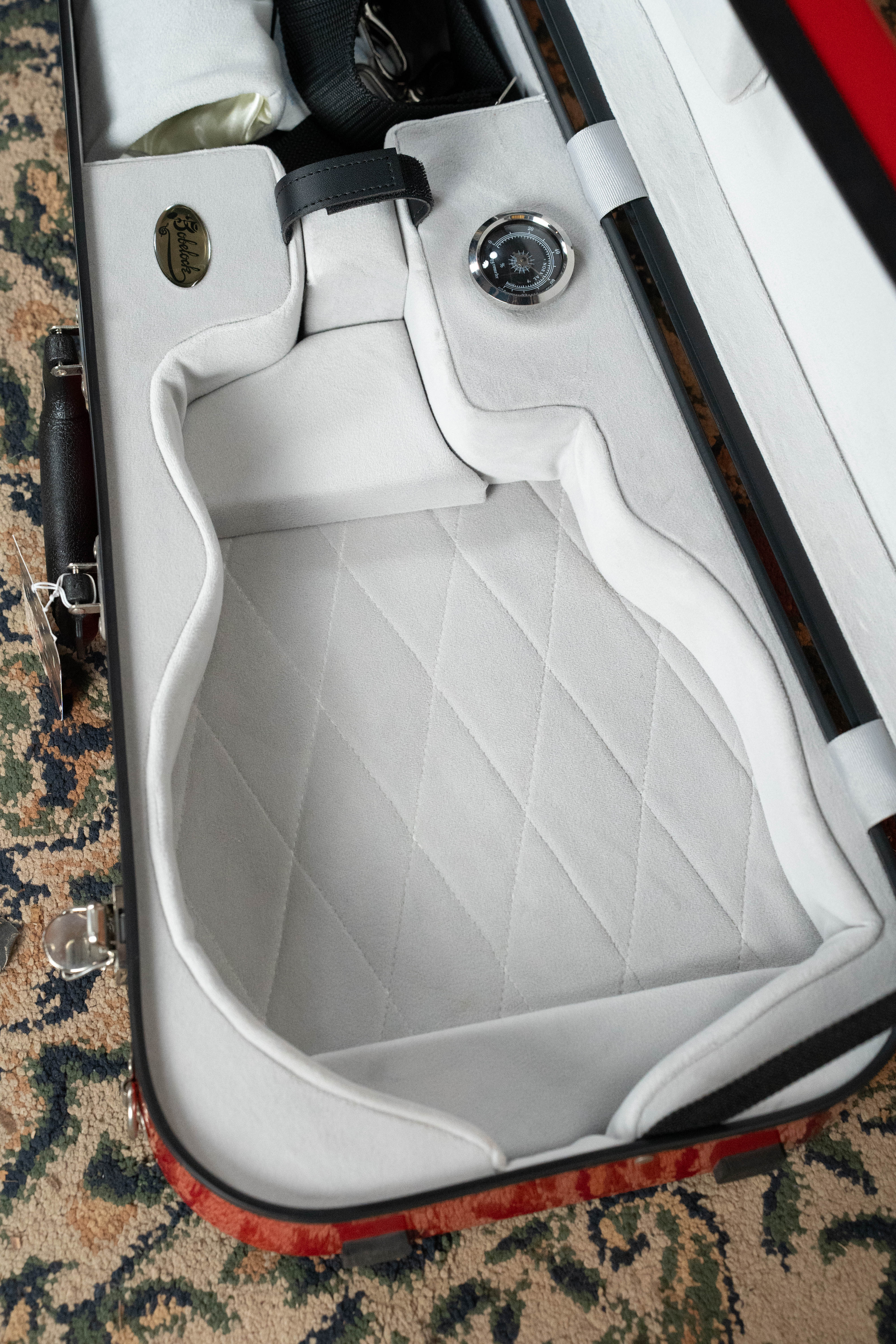 The Howard Core Bobelock Arrow Red/Gray F-Style Fiberglass Mandolin Case, with a soft quilted gray interior and molded sections for mandolin and accessories, is open and empty on a patterned carpet.
