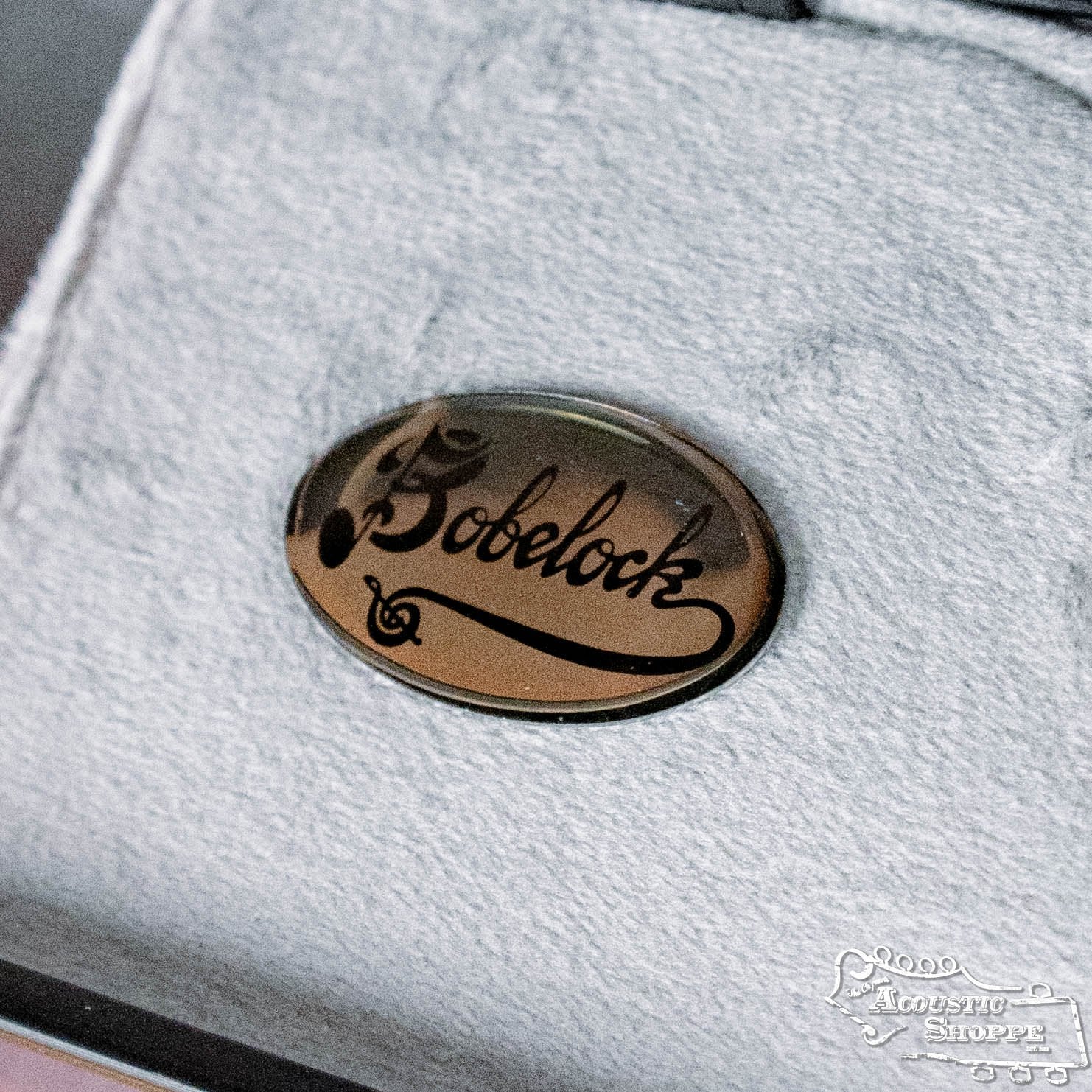 A close-up of a Bobelock Arrow Blue/Gray Fiberglass F-Style Mandolin Case B6-1029FBLS-BUGY pin with a swirl design, shown on soft gray fabric—ideal for labeling your case without needing a connector.