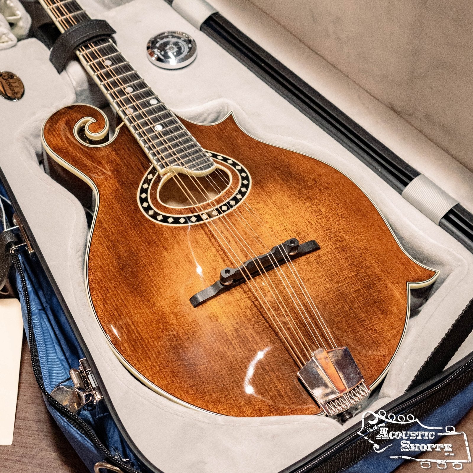 A mandolin rests in an open Bobelock Arrow Blue/Gray Fiberglass F-Style Mandolin Case (B6-1029FBLS-BUGY). The blue/gray case displays the Bobelock brand. No connector or spare cable is included.