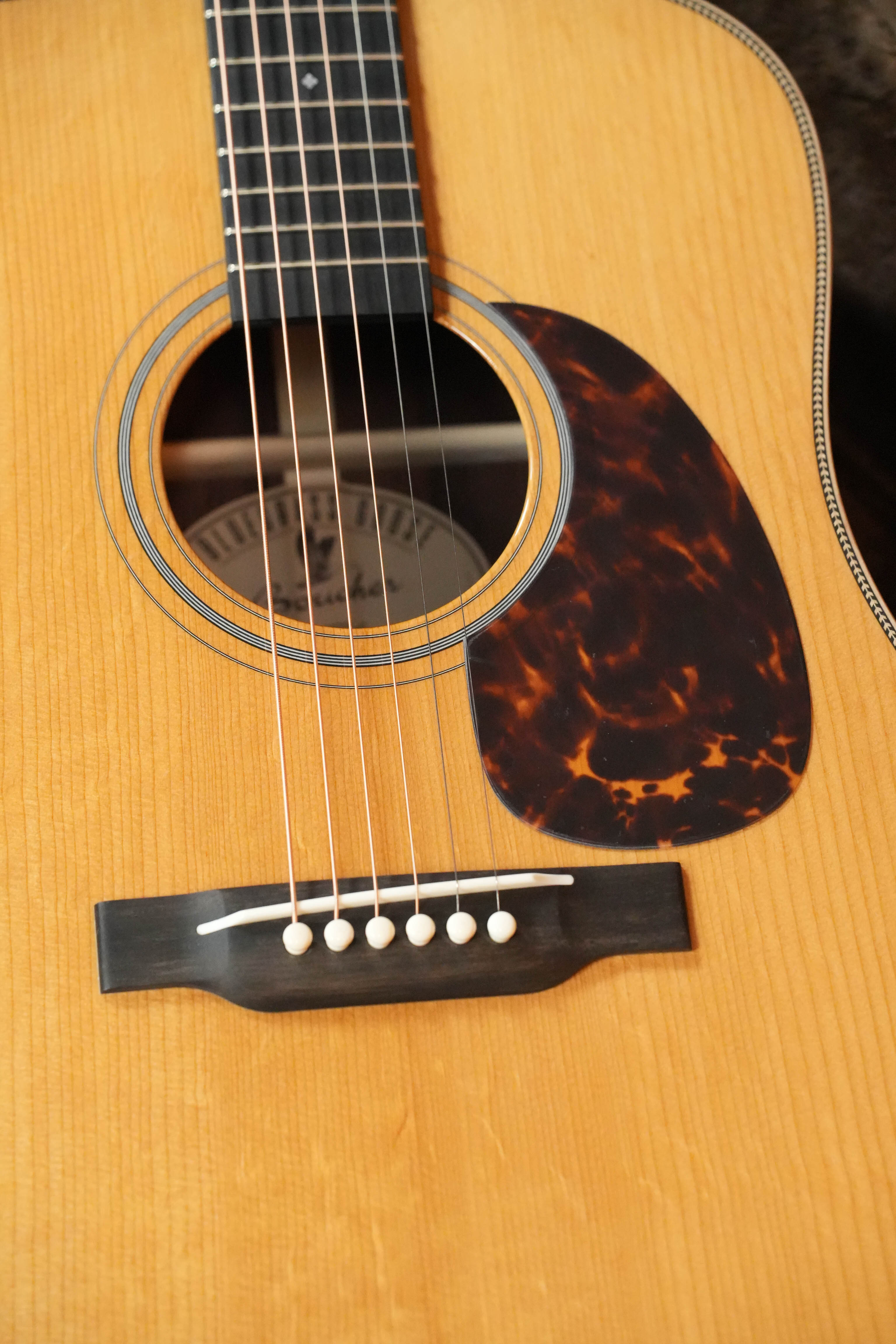 Close-up of the Boucher BG-152-G Adirondack/Rosewood Bluegrass Goose Dreadnought Acoustic Guitar #1098 by Boucher Guitars, highlighting its natural finish, sound hole, pickguard, bridge, and six strings—a bluegrass favorite.