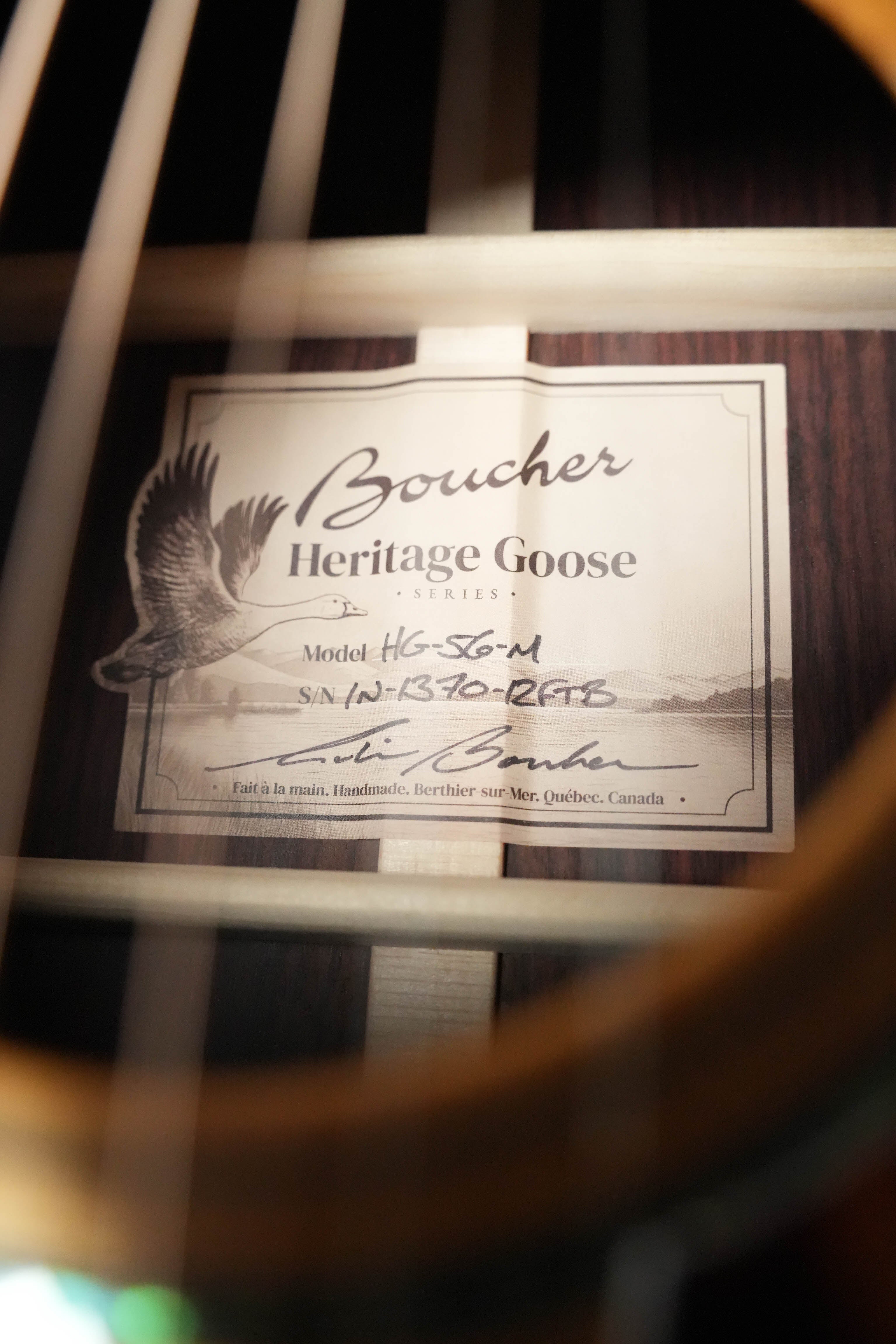 Close-up of a Boucher HG-56-M Adirondack/Rosewood OOO Acoustic Guitar #1370 label inside the soundhole at The Acoustic Shoppe, showing model, serial number, signature, and part of its torrefied Adirondack top with visible strings.