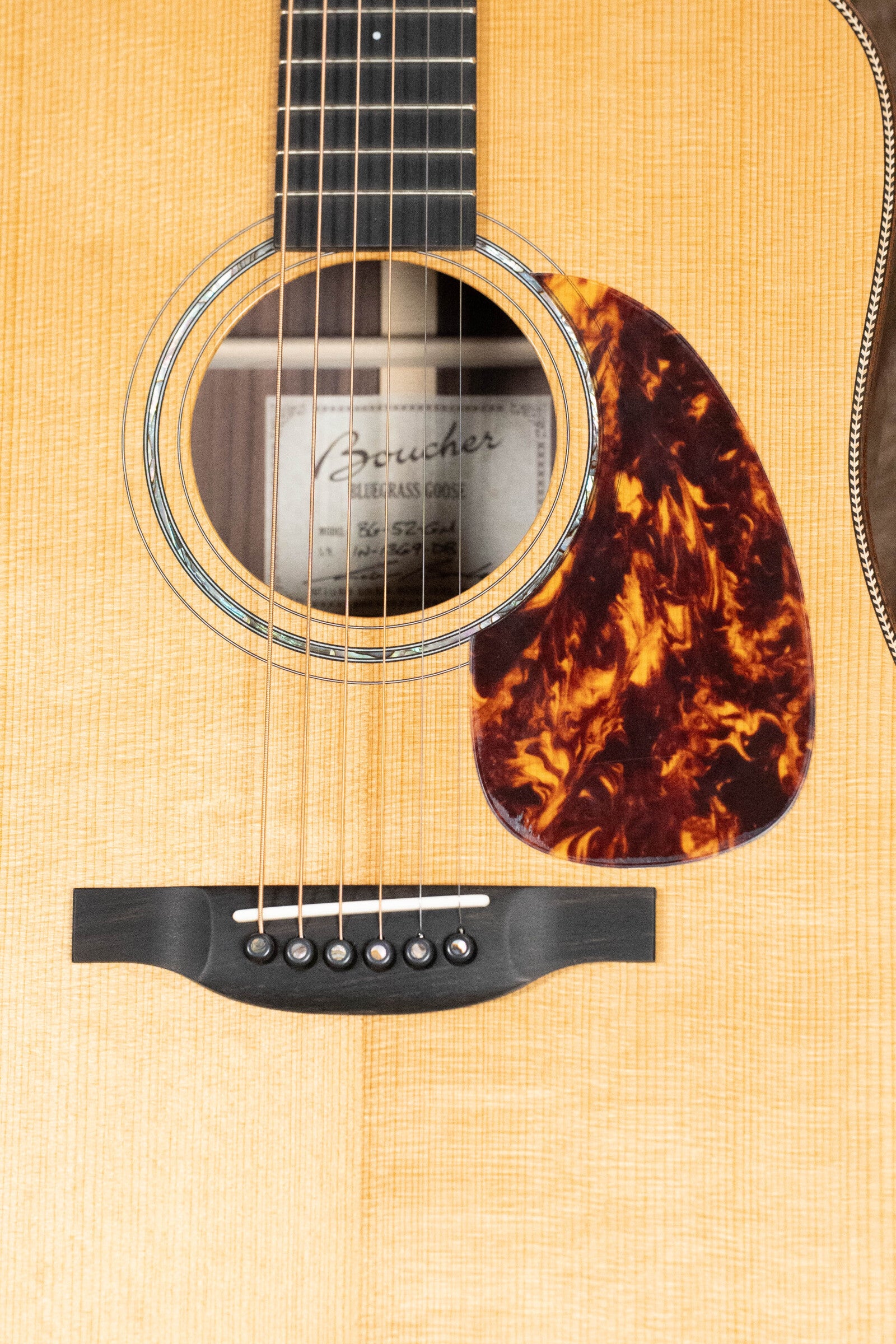 A close-up of the Boucher Guitars BG-52-GM Bluegrass Goose Dreadnought shows the sound hole, strings, tortoiseshell pickguard, and label—crafted with torrefied Adirondack red spruce top and East Indian rosewood back and sides.