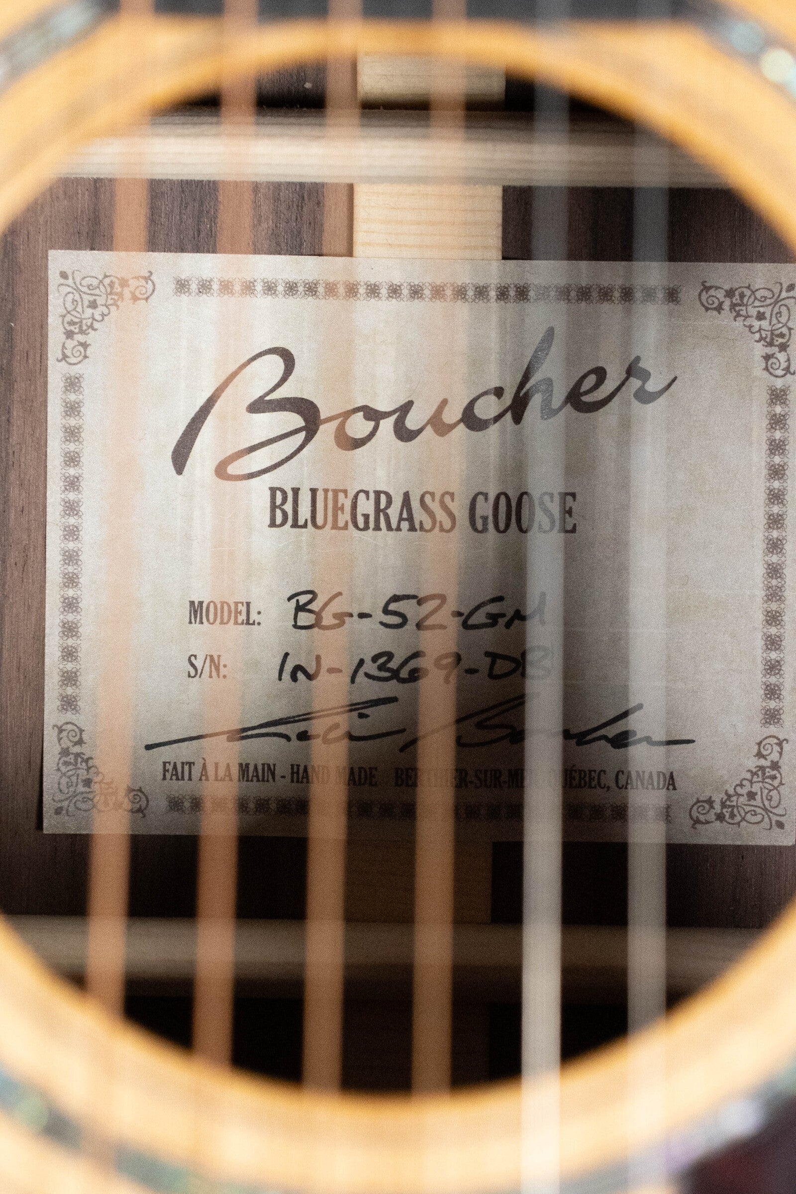 A close-up of the Boucher Guitars BG-52-GM Bluegrass Goose Series Dreadnought (#1369) showcases the label and gleaming strings; crafted with master grade torrefied Adirondack red spruce for a premium tone.