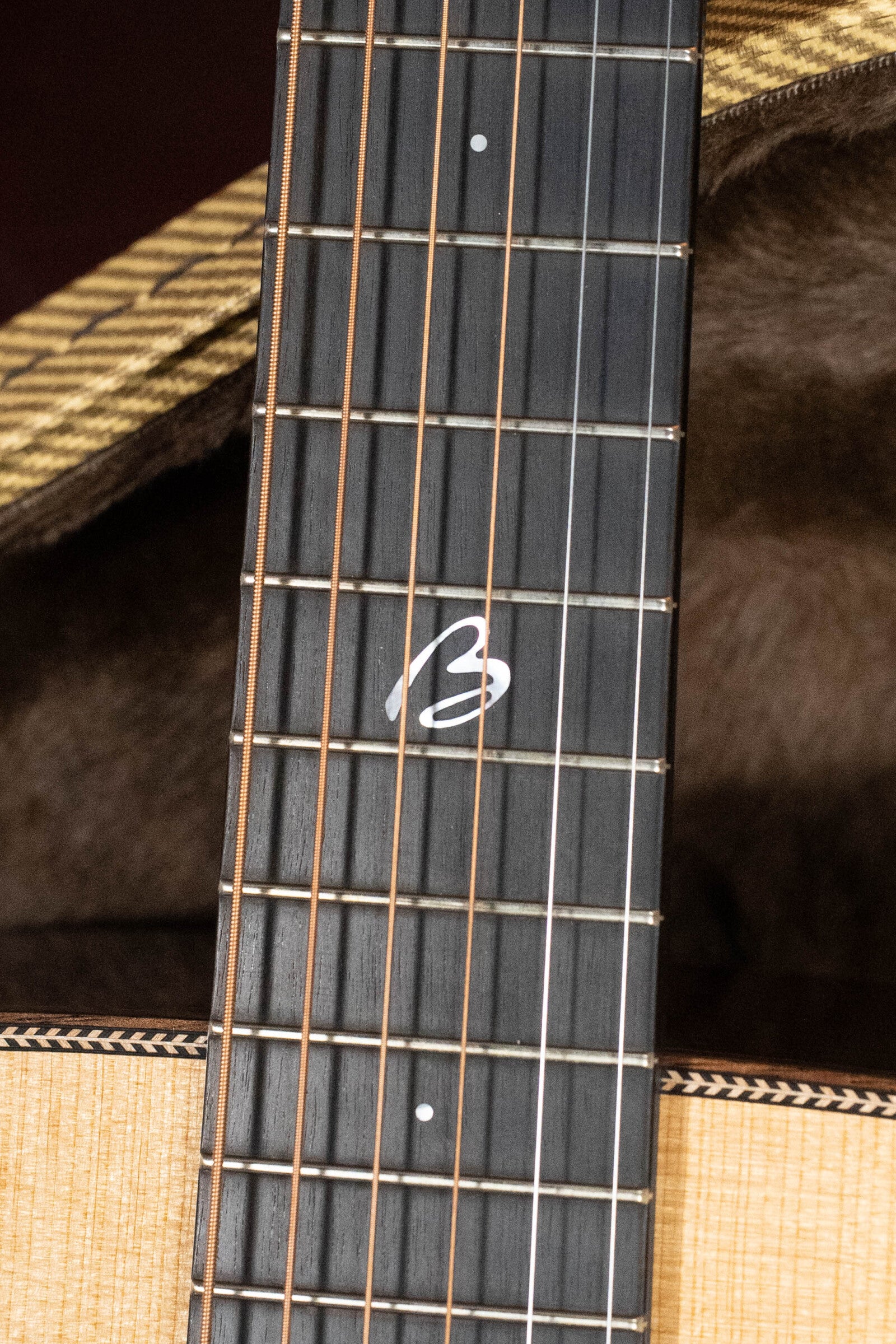 Close-up of a Boucher BG-52-GM Bluegrass Goose Series Dreadnought with metal frets, a stylized B inlay, and East Indian rosewood body. Plush-lined case partially visible. Crafted by Boucher Guitars.