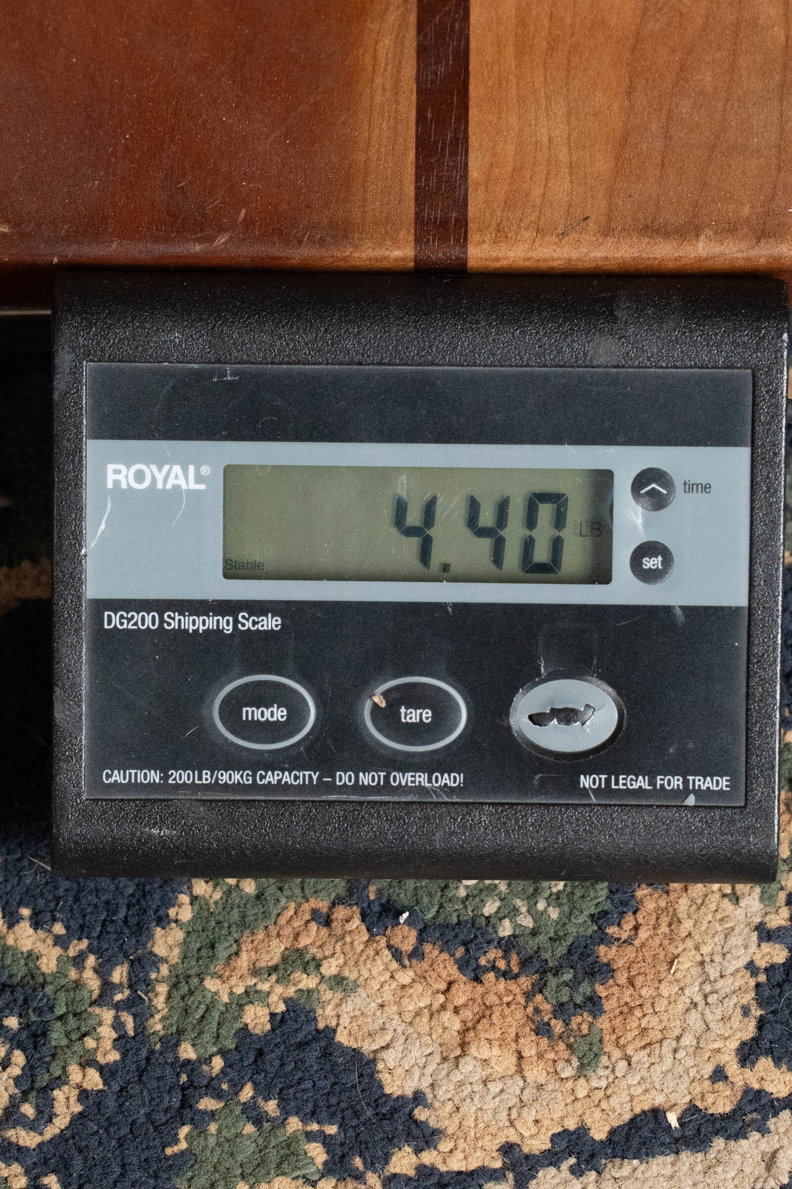 A digital shipping scale shows a weight of 4.40 pounds. Nearby, brown furniture echoes the deep hues of the Boucher Guitars BG-52-GM Bluegrass Goose Series Dreadnought’s East Indian Rosewood back and sides.