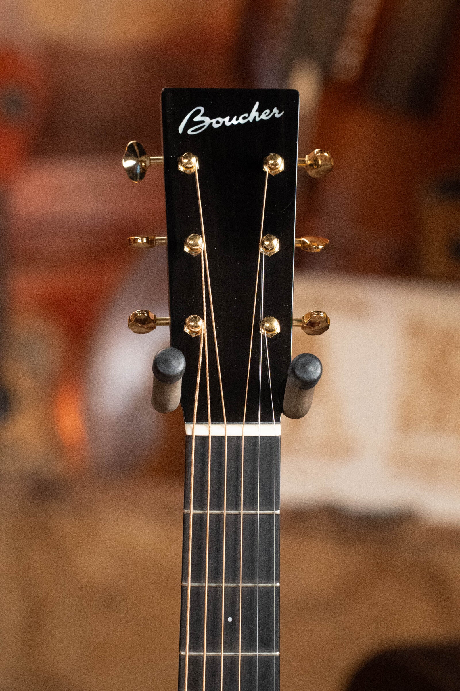 Close-up of a Boucher Guitars BG-52-GM Bluegrass Goose Series Dreadnought headstock with gold tuning pegs and logo. Master grade Adirondack red spruce/East Indian rosewood build, designed for bluegrass players, shown on a stand with blurred background.