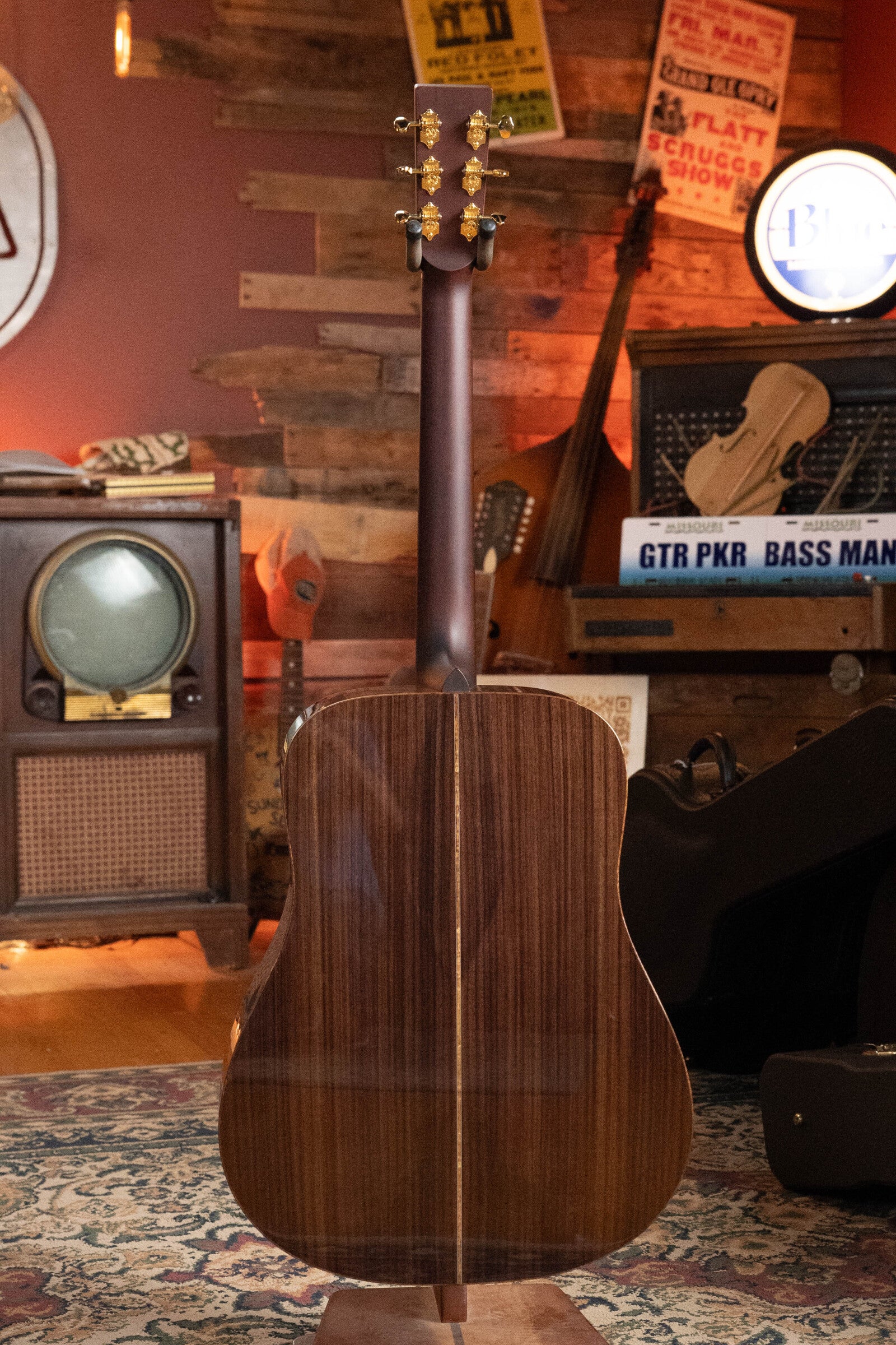 The Boucher Guitars BG-52-GM Bluegrass Goose Series Dreadnought #1369, crafted from master grade Adirondack red spruce and East Indian rosewood, is displayed from the back in a vintage-style room with retro decor.