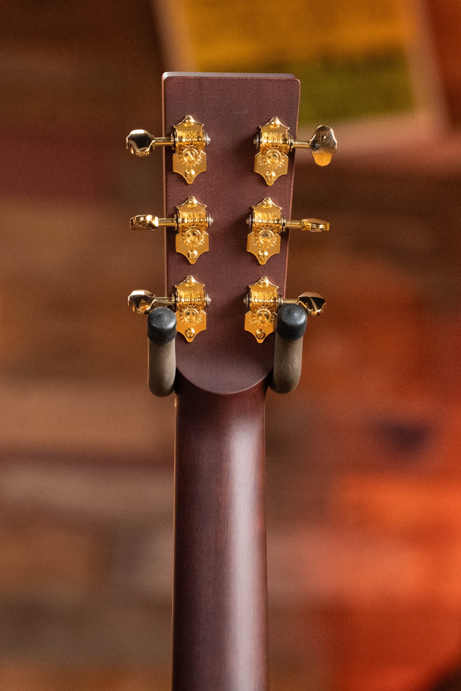 The Boucher BG-52-GM Bluegrass Goose Dreadnought Acoustic Guitar by Boucher Guitars features six gold tuners on an Indian rosewood headstock, set against a warm, blurred background that highlights its elegant finish.