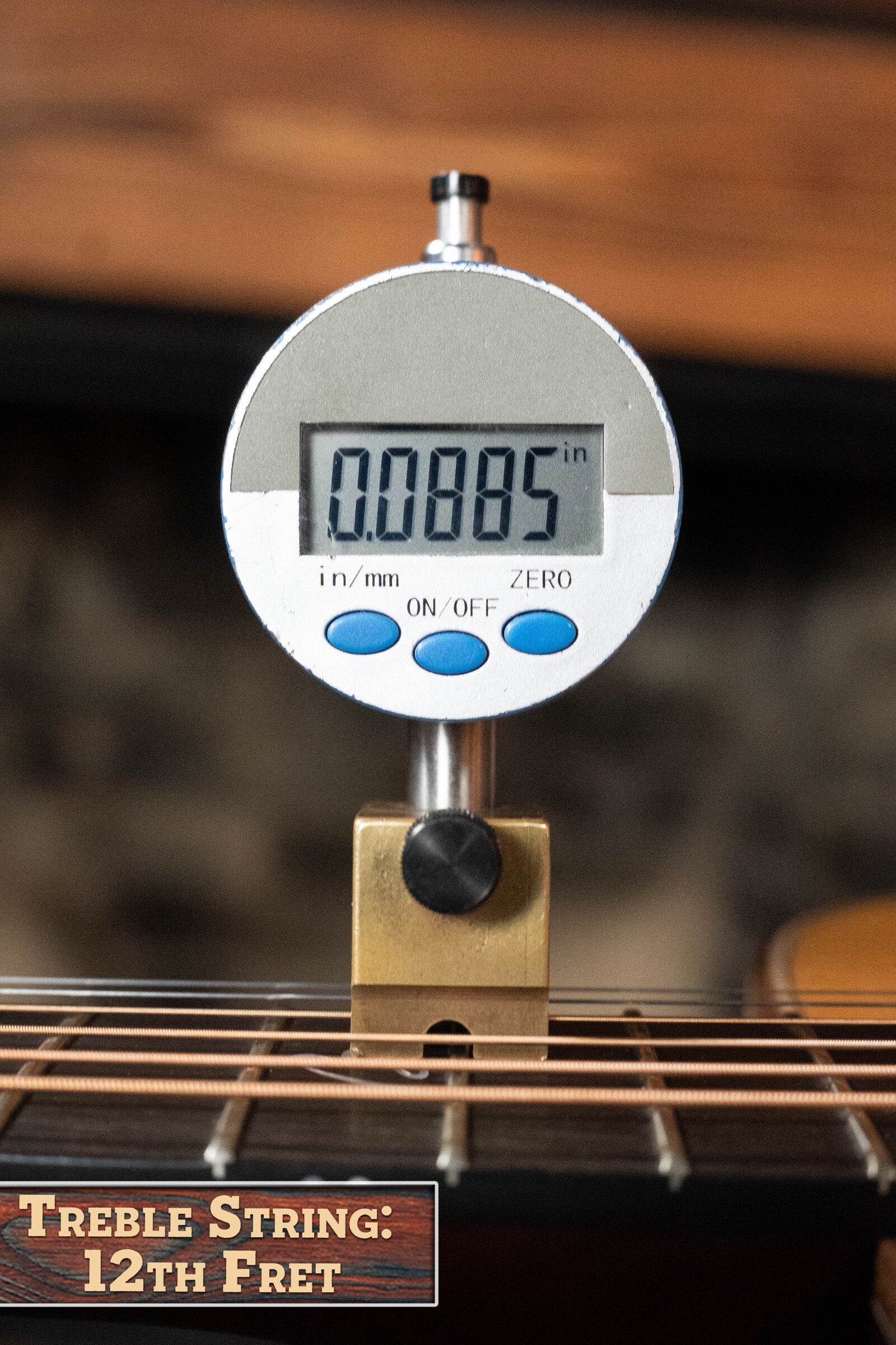 A digital gauge shows a 0.0085-inch string height at the 12th fret of a Boucher BG-52-GM Bluegrass Goose Series Dreadnought by Boucher Guitars, with a sign below reading Treble String: 12th Fret.