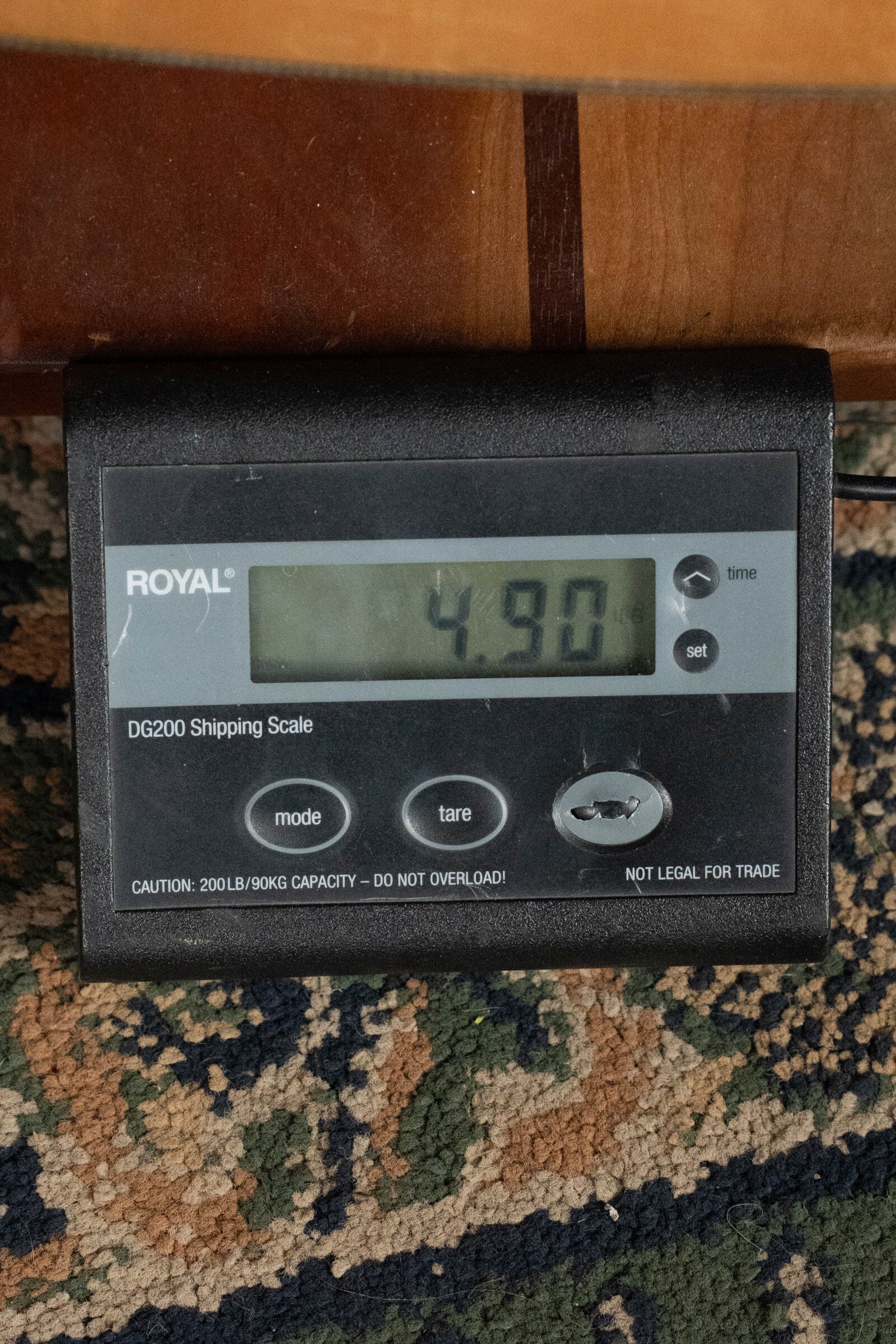 A digital shipping scale shows 4.90 pounds. The scale rests on carpet, with a wooden surface—like the Old-Growth Alaskan Sitka Spruce found in the Bourgeois D Vintage/TS Touchstone Series Dreadnought Acoustic Guitar #7014—above it.