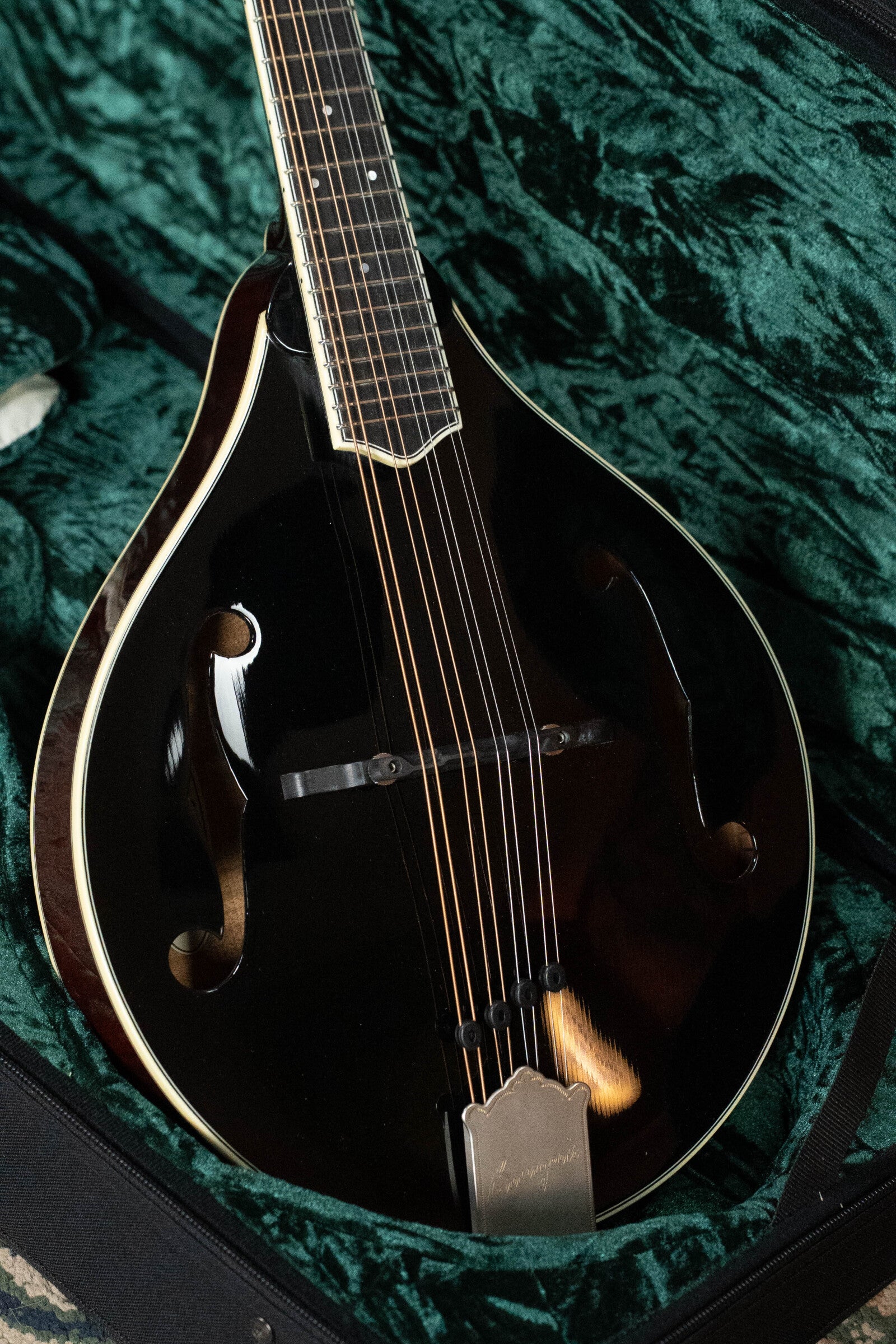The Bourgeois M5-A-BT Aged-Tone Black Top A-Style Mandolin #2020 by Bourgeois features a glossy black finish, F-holes, metal strings, and a decorative tailpiece, resting in a green velvet-lined hard case.