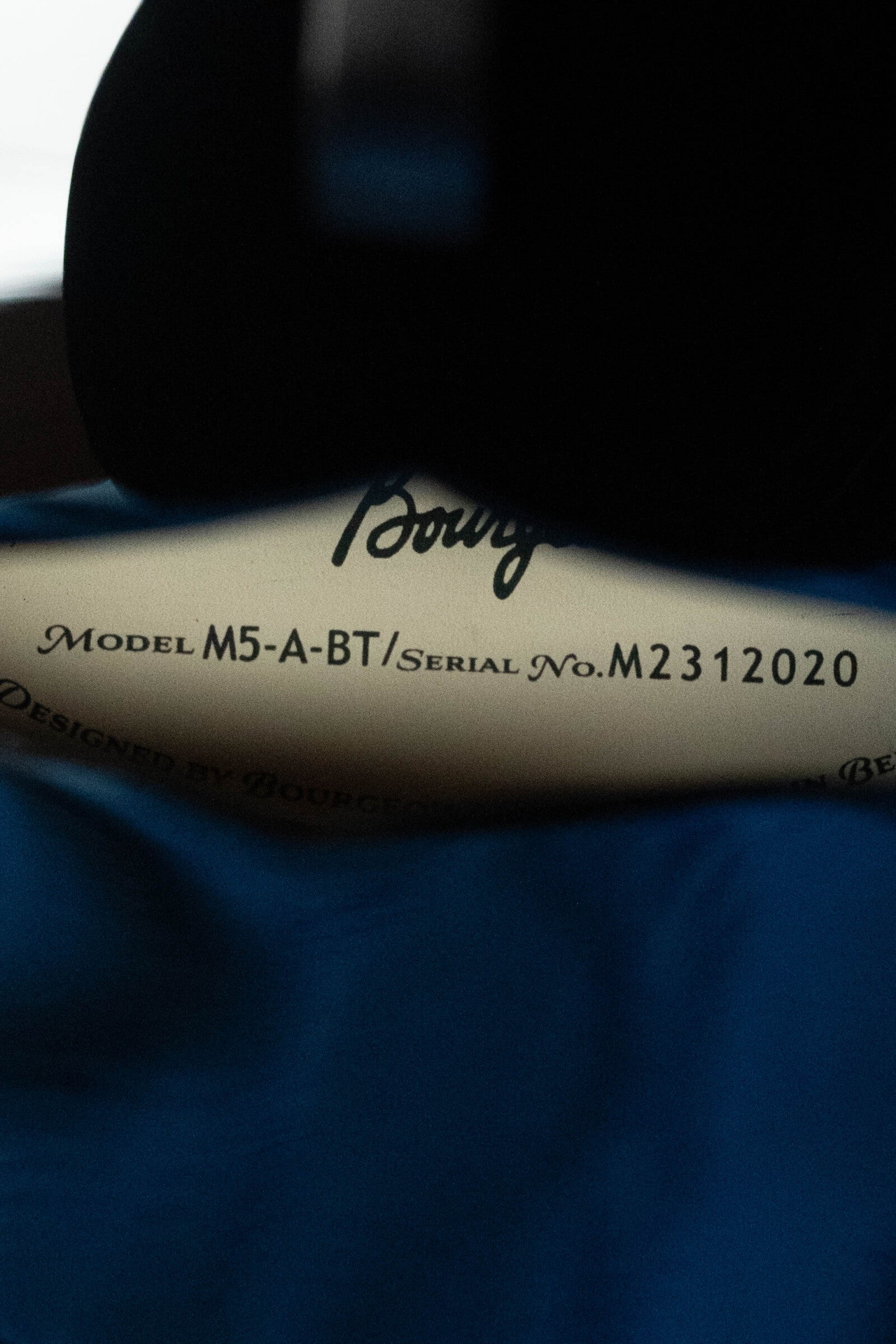Close-up of a label reading Model M5-A-BT / Serial No. M2312020, in black text on a light surface partly covered by blue cloth; Bourgeois is partially visible, identifying this as a Bourgeois M5-A-BT Aged-Tone Black Top A-Style Mandolin #2020.