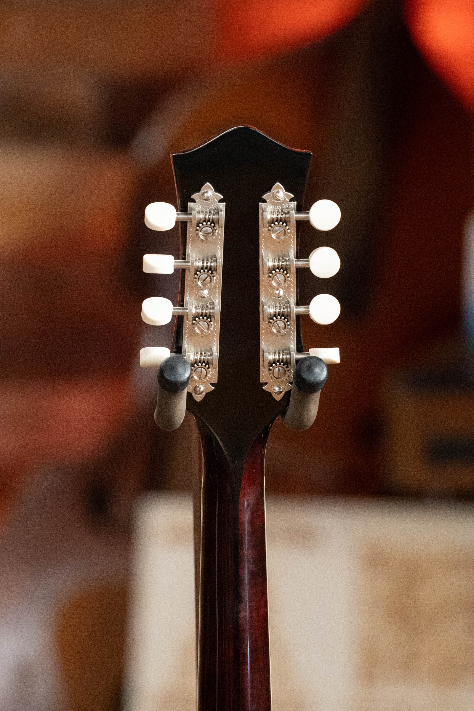 The image shows the back of the Bourgeois M5-A-BT Aged-Tone Black Top A-Style Mandolin #2020 headstock with eight tuning pegs and visible metal mechanisms. The background is blurred.