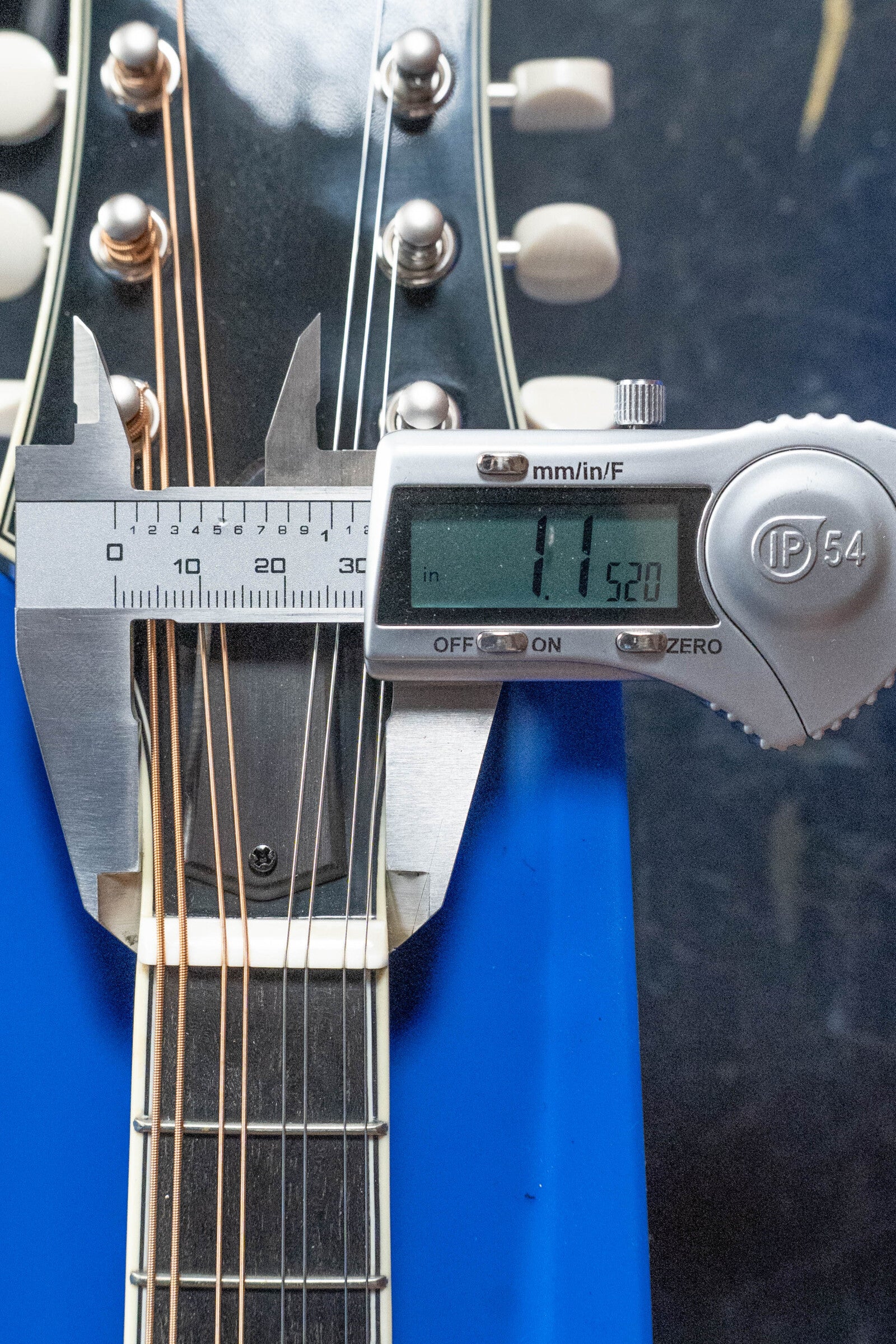 A digital caliper shows 1.1520 inches between the outer strings on a Bourgeois M5-A-BT Aged-Tone Black Top A-Style Mandolin #2020 headstock, with partial views of its headstock and tuning pegs.