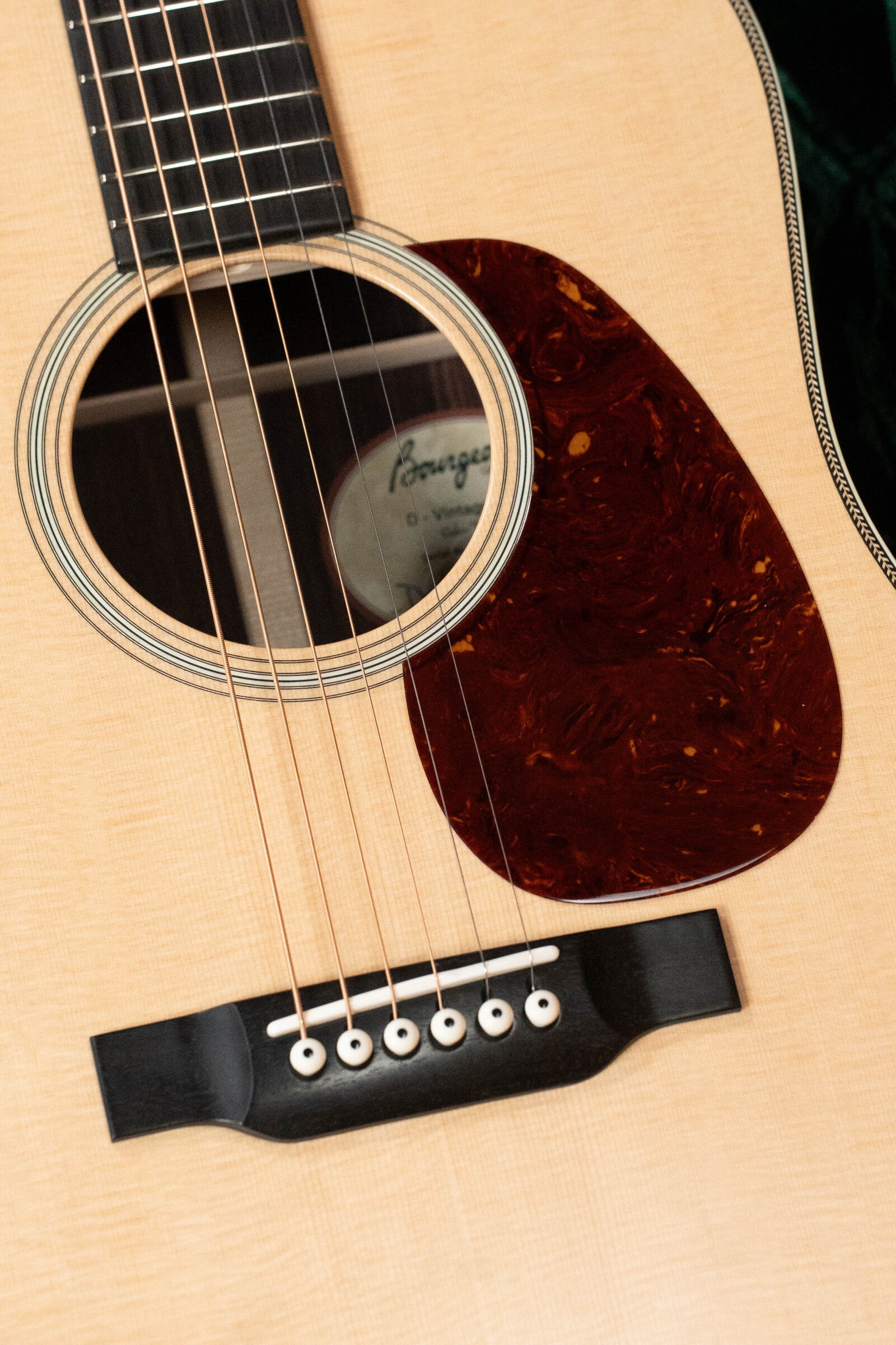 Close-up of the Bourgeois PSV-D-S Professional Series Sitka/Rosewood Vintage Satin Dreadnought Acoustic Guitar #1124, highlighting the sound hole, strings, wooden bridge, marbled brown pickguard, and stunning Sitka spruce top.