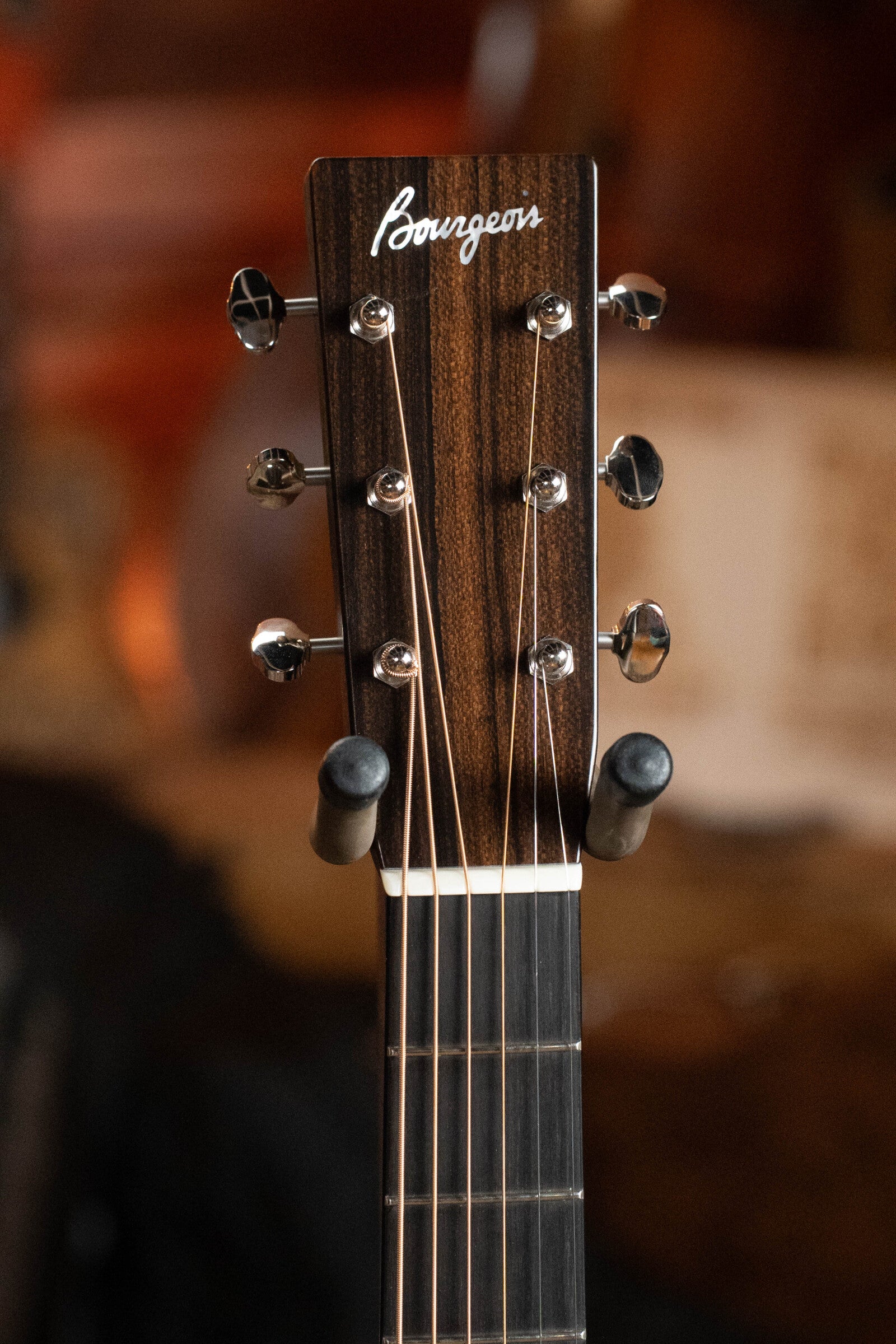 Close-up of the Bourgeois PSV-D-S Professional Series Sitka/Rosewood Dreadnought Guitar (#1124) headstock with silver tuning pegs and logo, set against a blurred, warm-toned background.