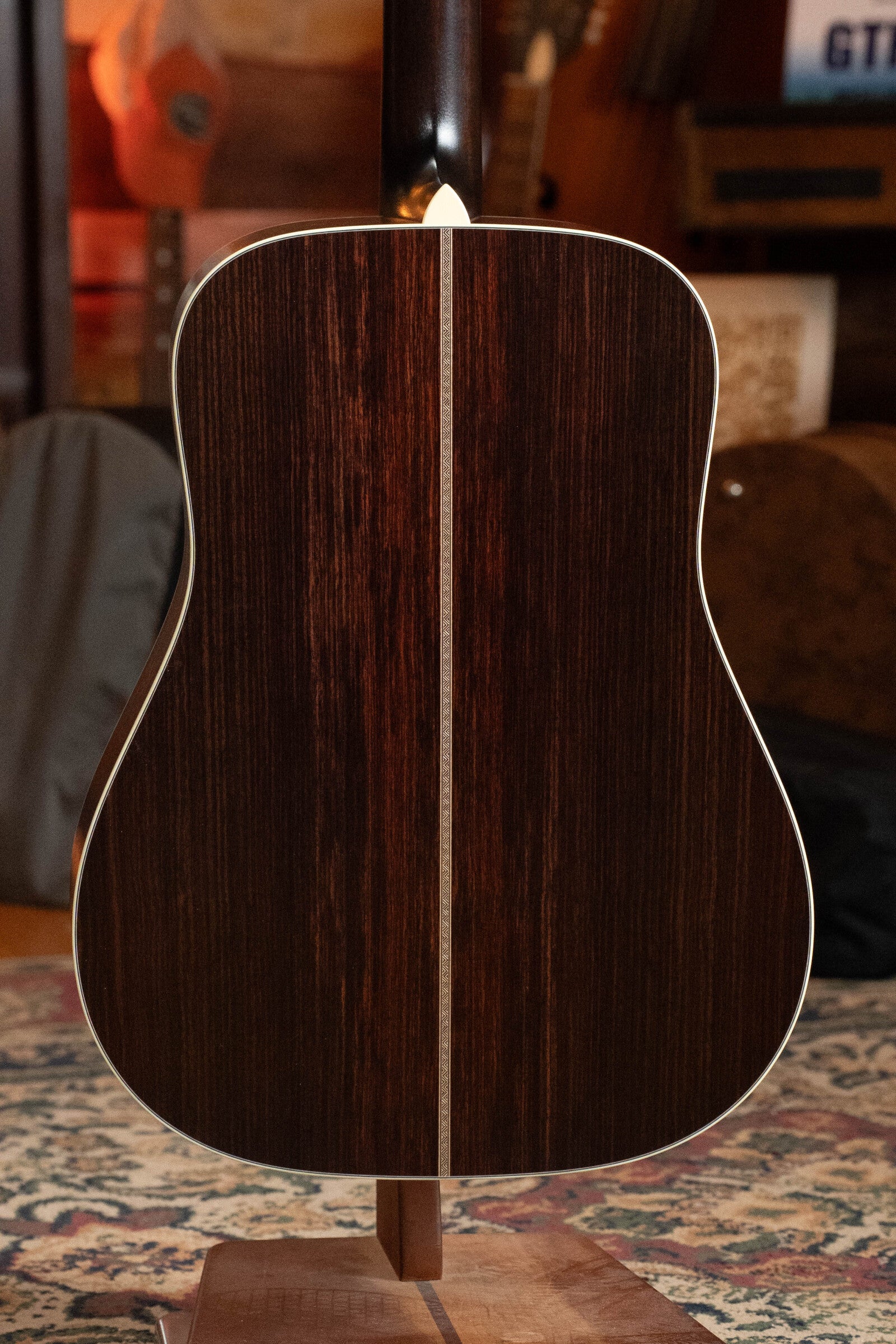 The image shows the back of a Bourgeois PSV-D-S Professional Series Sitka/Rosewood Vintage Satin Dreadnought Acoustic Guitar (#1124) with an Indian rosewood finish, center strip, and light binding, resting on a patterned rug.