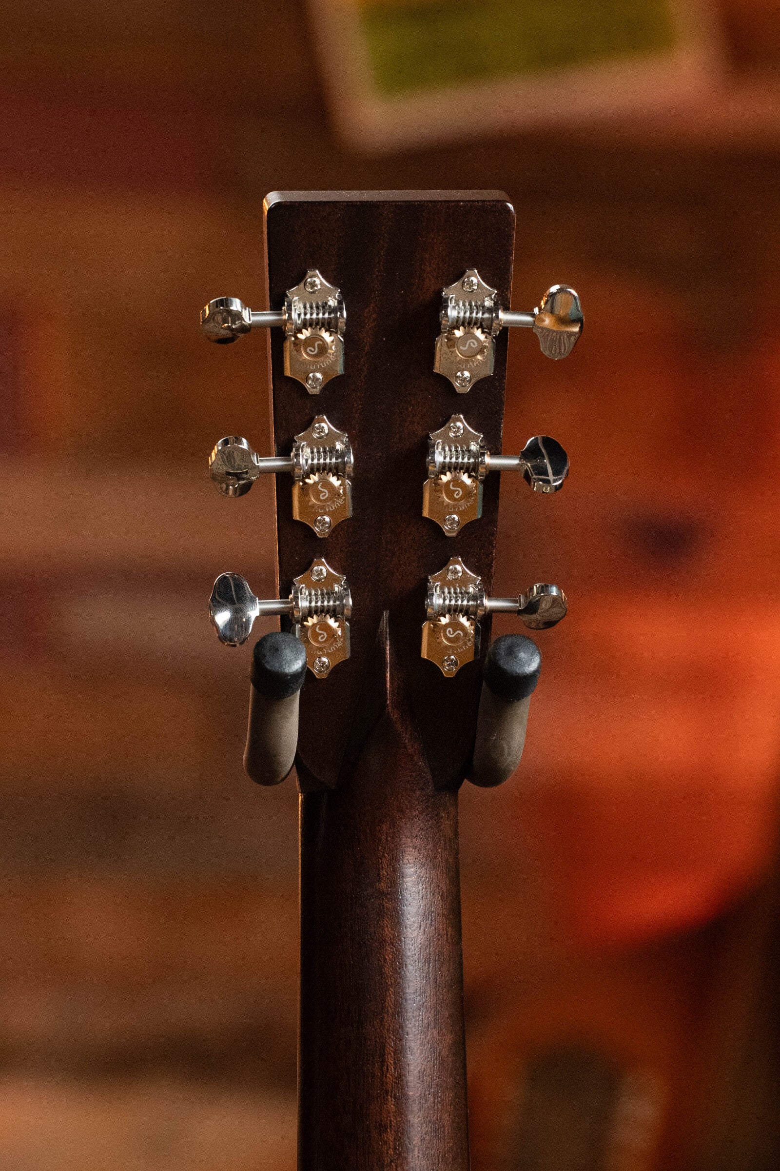 Close-up of the Bourgeois PSV-D-S Professional Series Sitka/Rosewood Vintage Satin Dreadnought Acoustic Guitar #1124 headstock, showing six silver tuners against a warm, blurred background; the guitar rests on a stand.