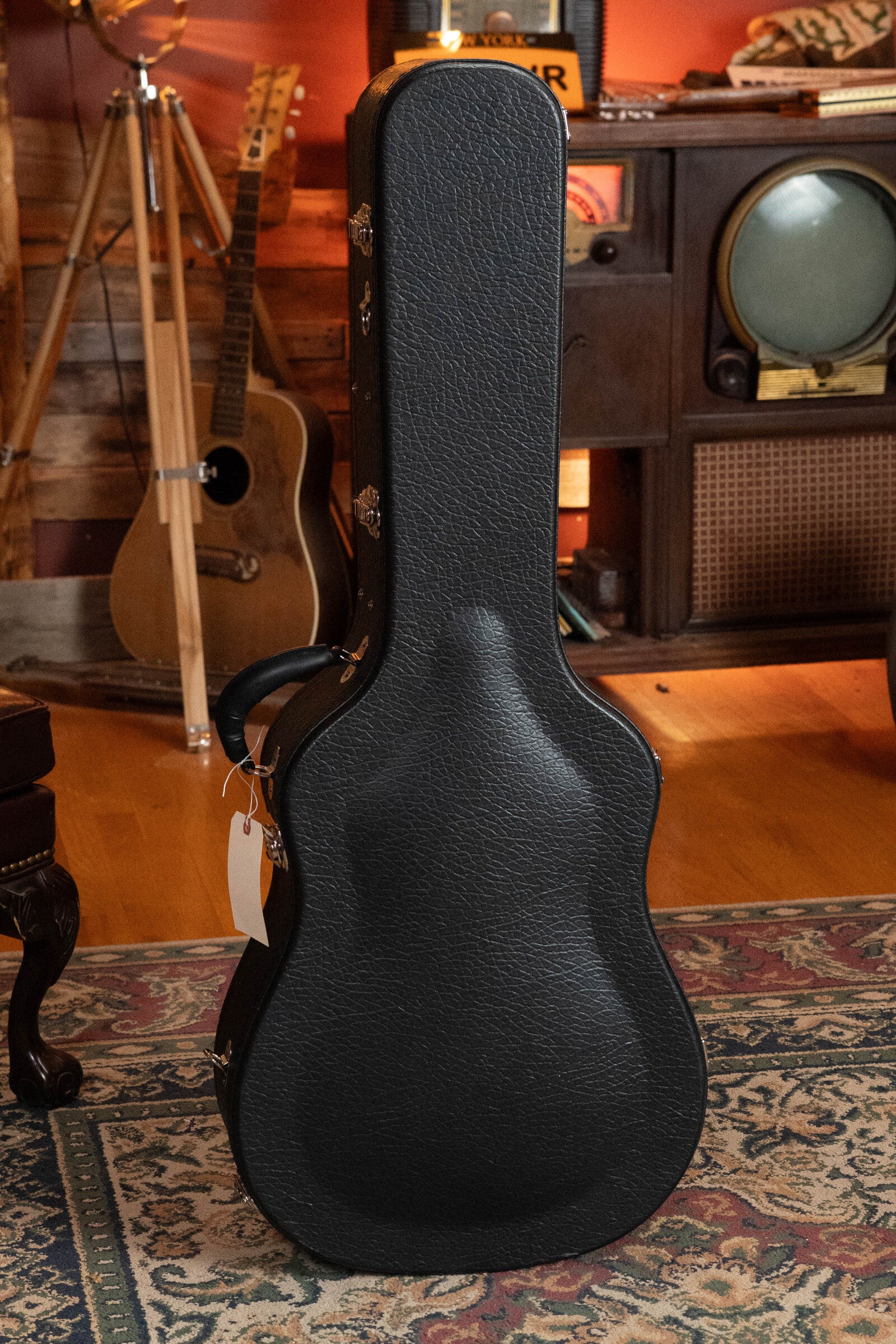 A Bourgeois PSV-D-S Professional Series Sitka/Rosewood Vintage Satin Dreadnought Acoustic Guitar (#1124) stands upright in its black hard case on a patterned rug, with wooden floors, vintage TV, and tripod in the cozy room.
