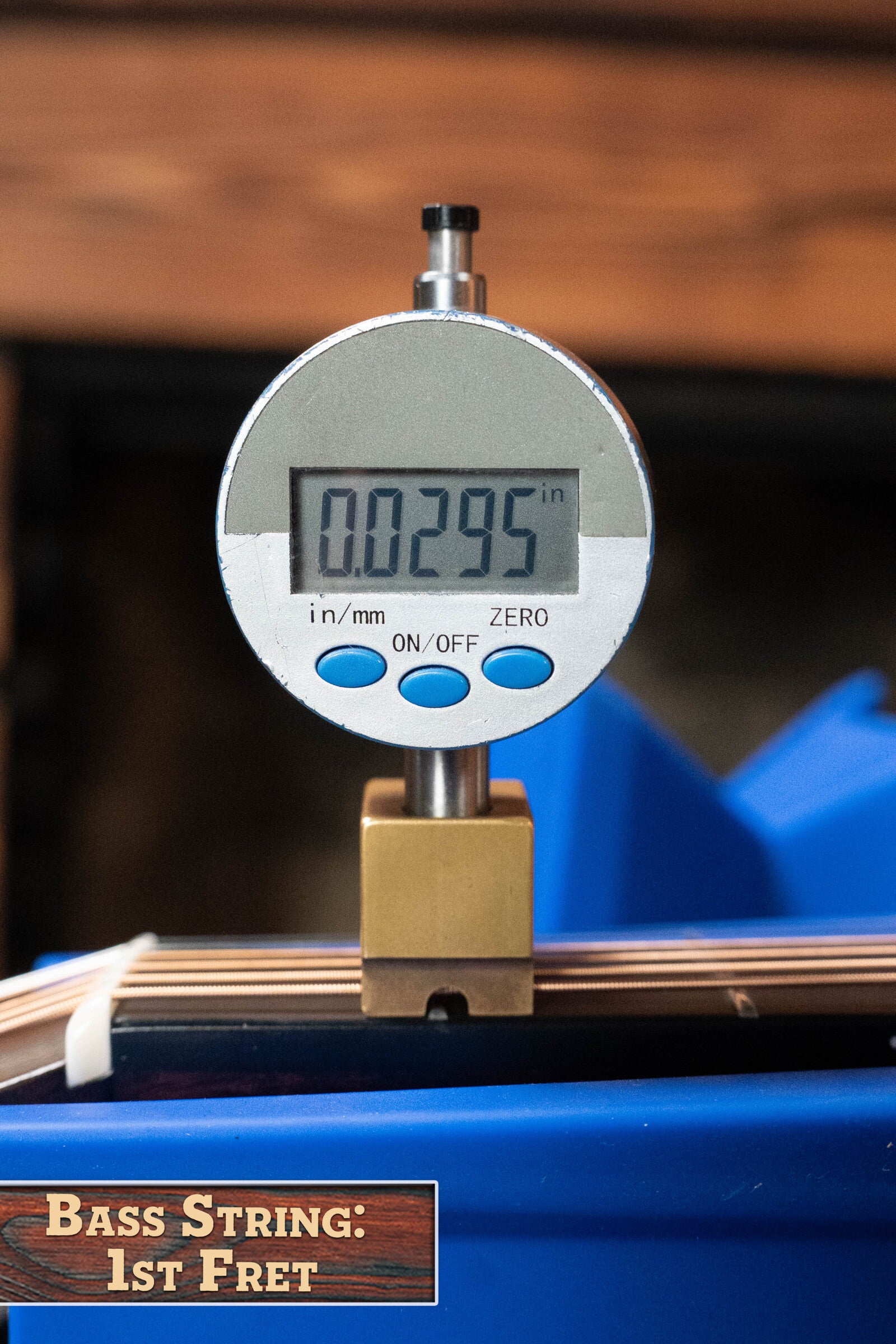 A digital gauge reads 0.0295 inches when measuring the bass string height at the 1st fret of a Bourgeois PSV-D-S Professional Series Sitka/Rosewood Vintage Satin Dreadnought Acoustic Guitar #1124, with a sign labeled Bass String: 1st Fret below.